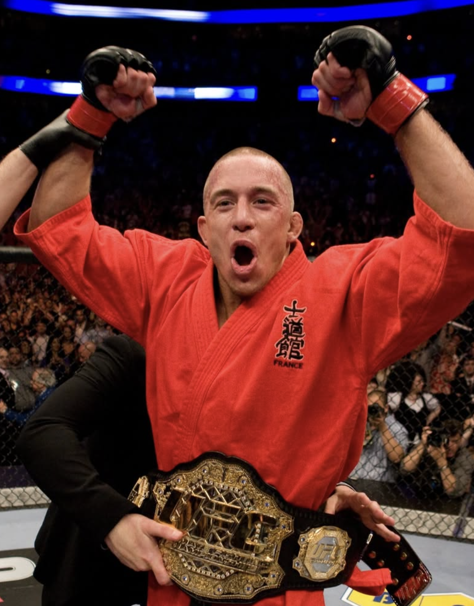 A victorious martial artist in a red robe triumphantly holds a championship belt, surrounded by an enthusiastic crowd.