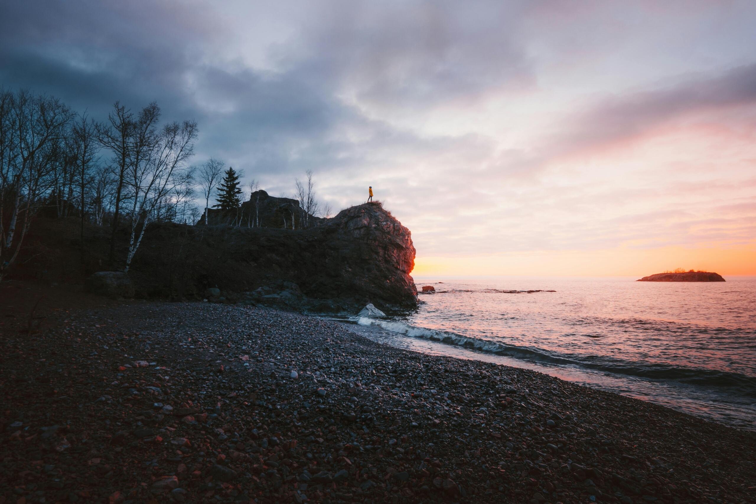 A rocky cliff juts out into a lake at sunset.
