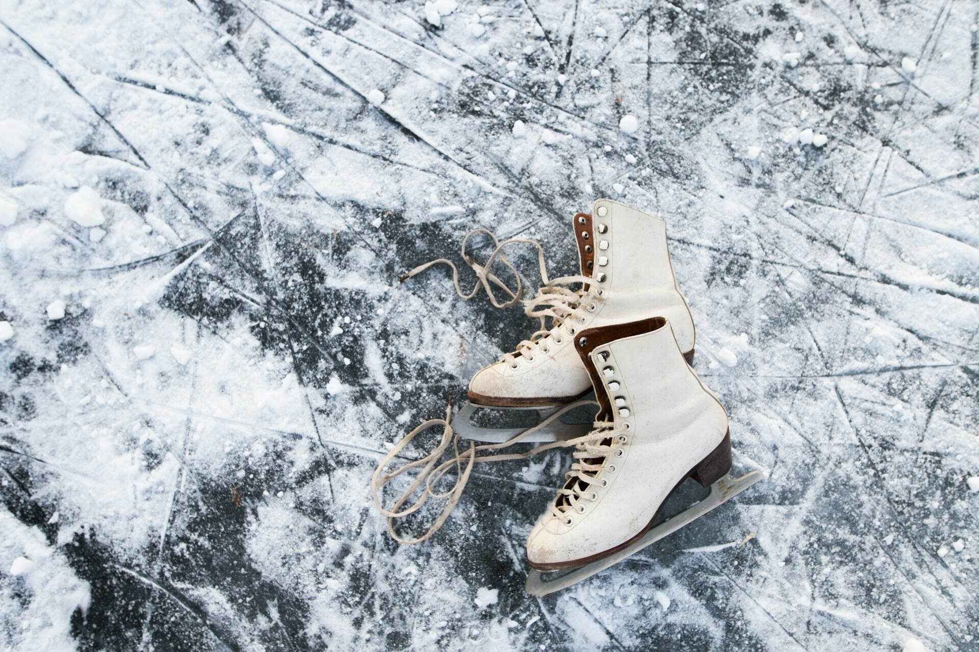 A pair of worn white ice skates rests on a snowy, scratched ice surface, with loose laces coiled beside them.