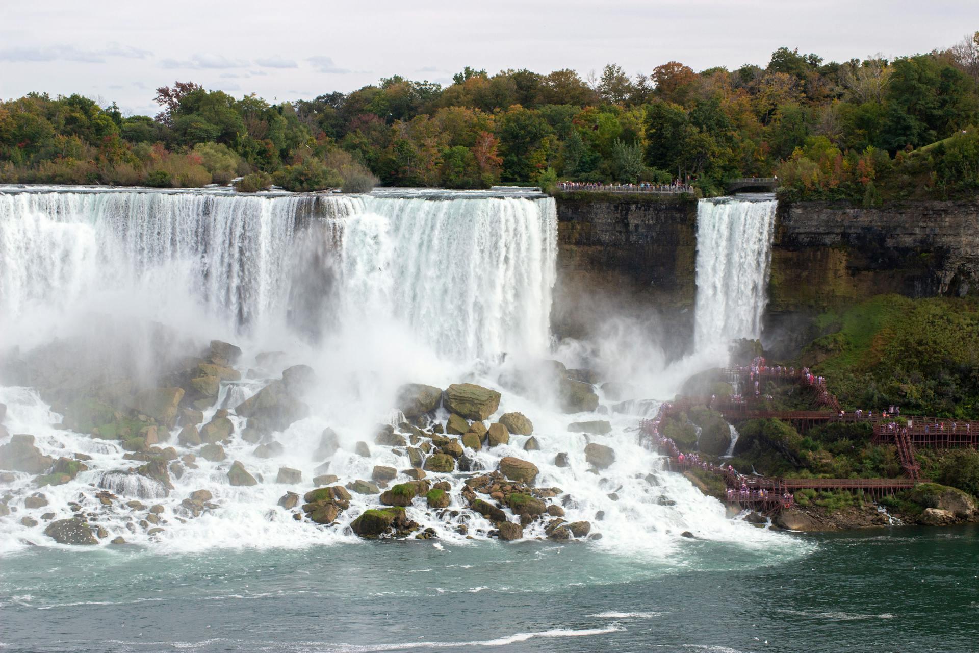 Niagara Falls cascades powerfully over rocky cliffs, shrouded in mist, with visitors along the observation paths admiring the natural wonder.