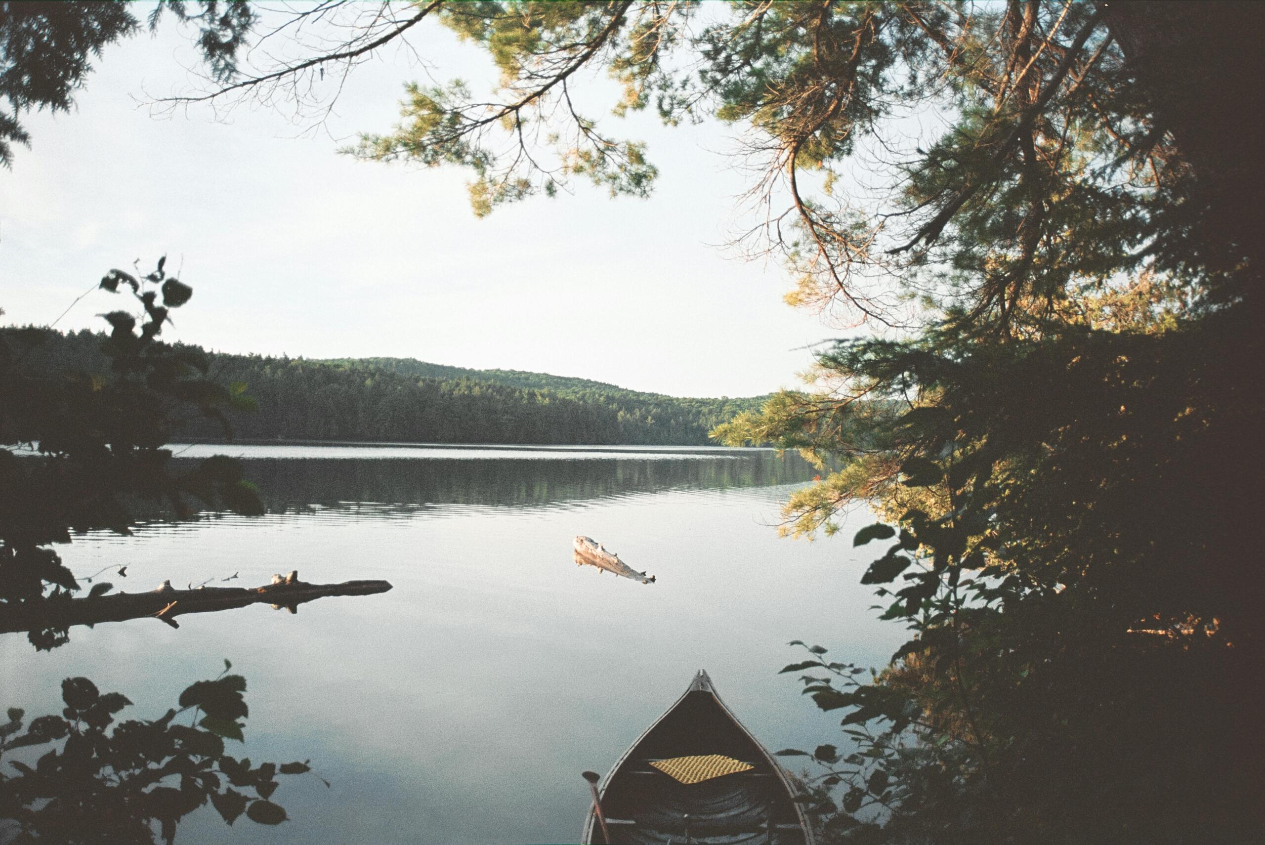 A canoe can is visble on a calm lake surrounded by forests.