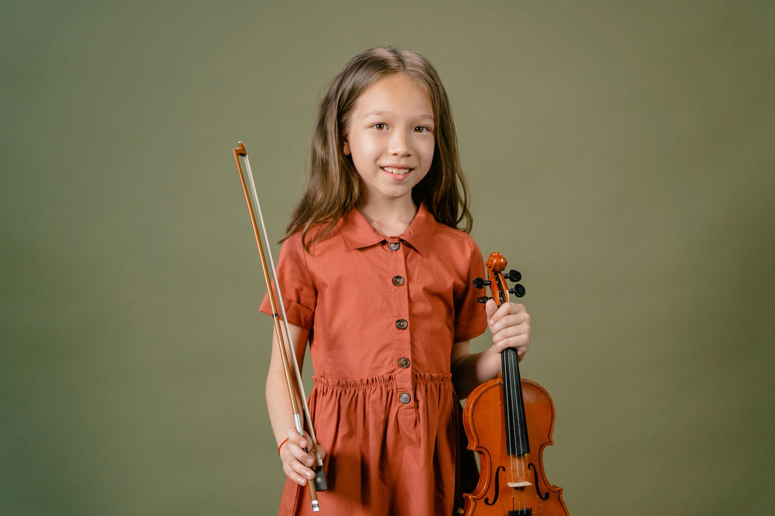 A young girl holds a violin and bow in her hands.