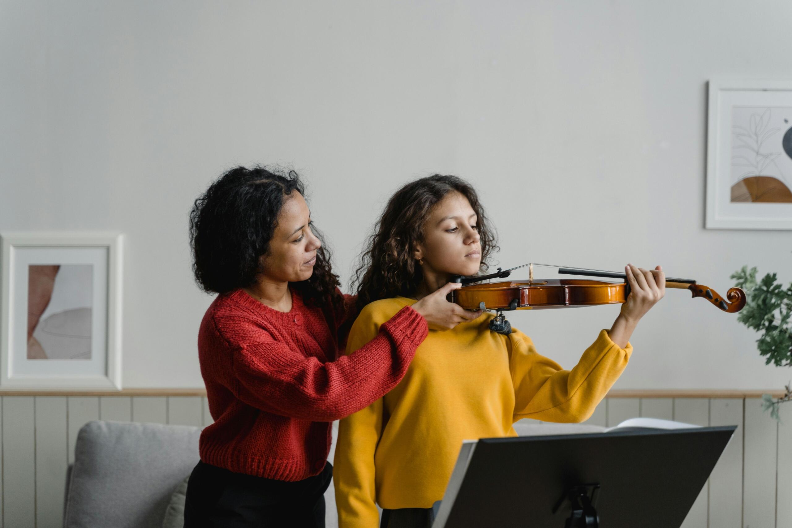 A music teacher holds a violin in place for a student.