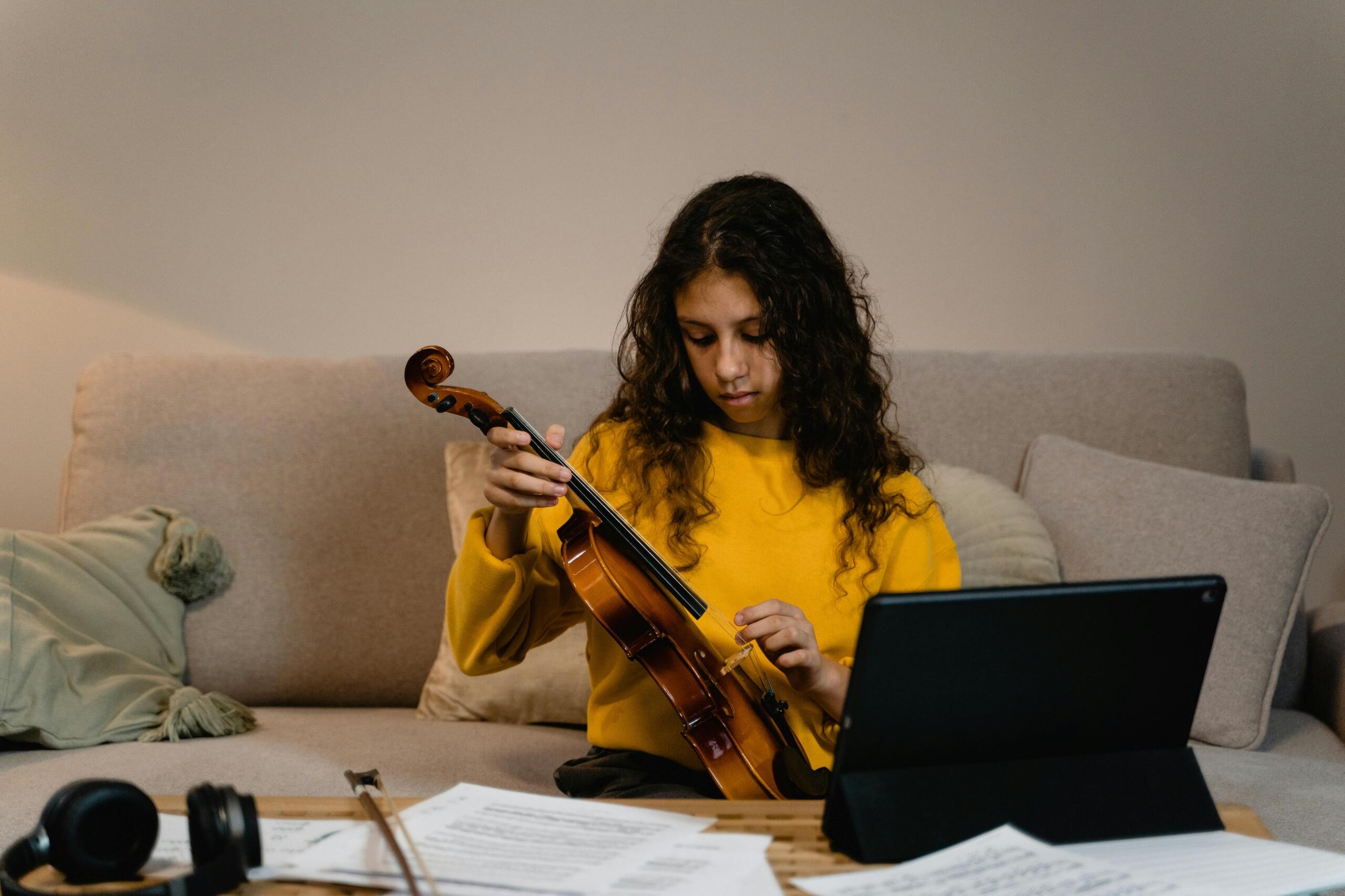 A girl adjusts a violin in her home. A computer is in front of her.