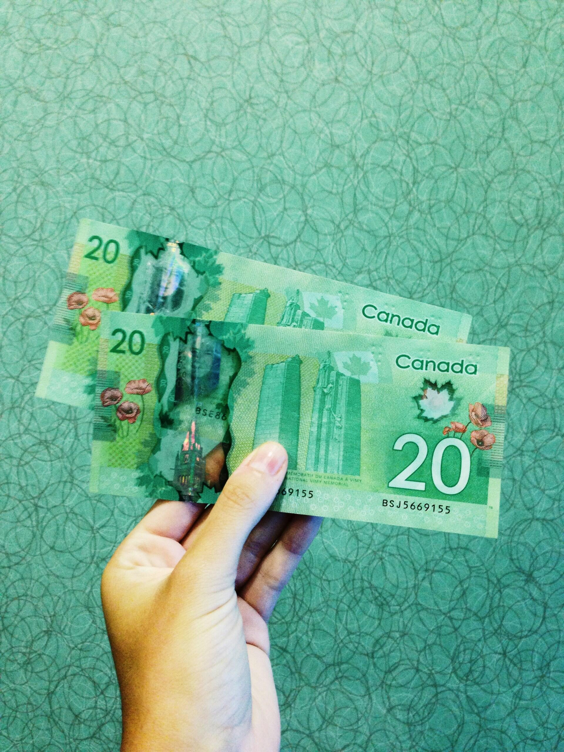 someone holding two green 20CAD bills