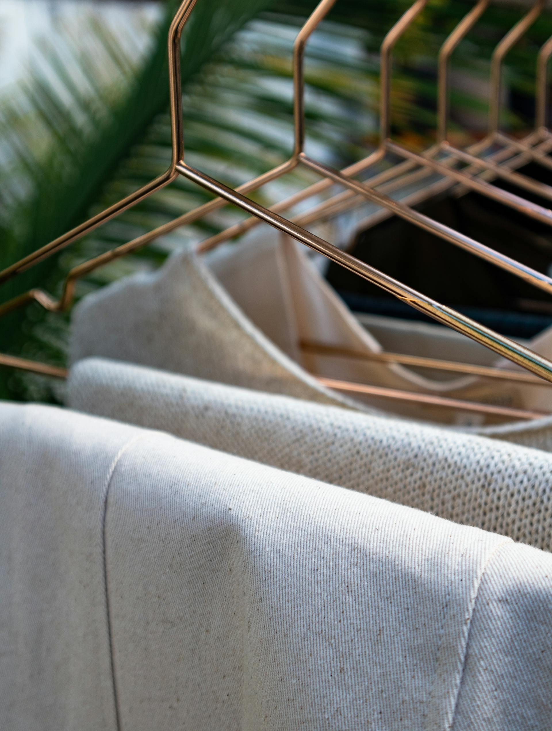 Close-up of a copper wire clothing rack displaying hanging light-colored fabric and a backdrop of lush green foliage.