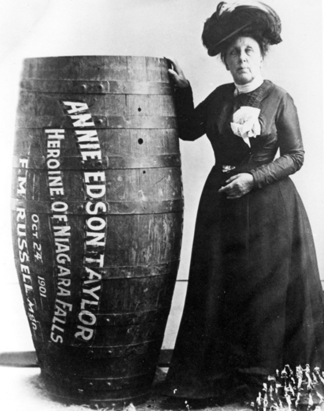 Annie Edson Taylor stands next to a large wooden barrel labeled with her name and details of her 1901 Niagara Falls stunt.