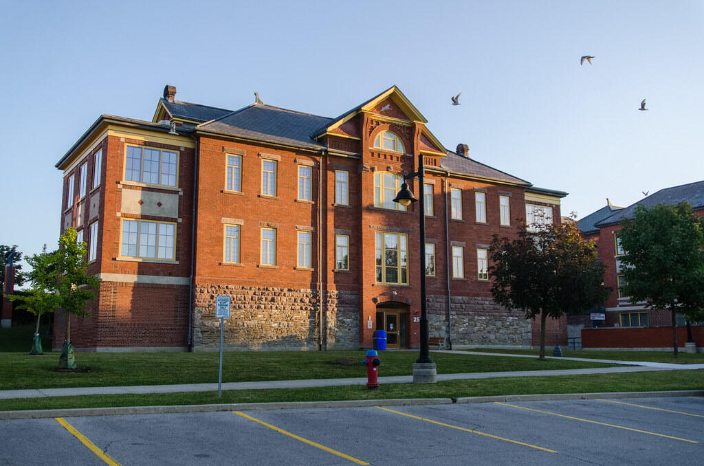 Front view of Humber College’s historic red-brick building with large windows and a central entrance, captured during golden hour with birds flying overhead.