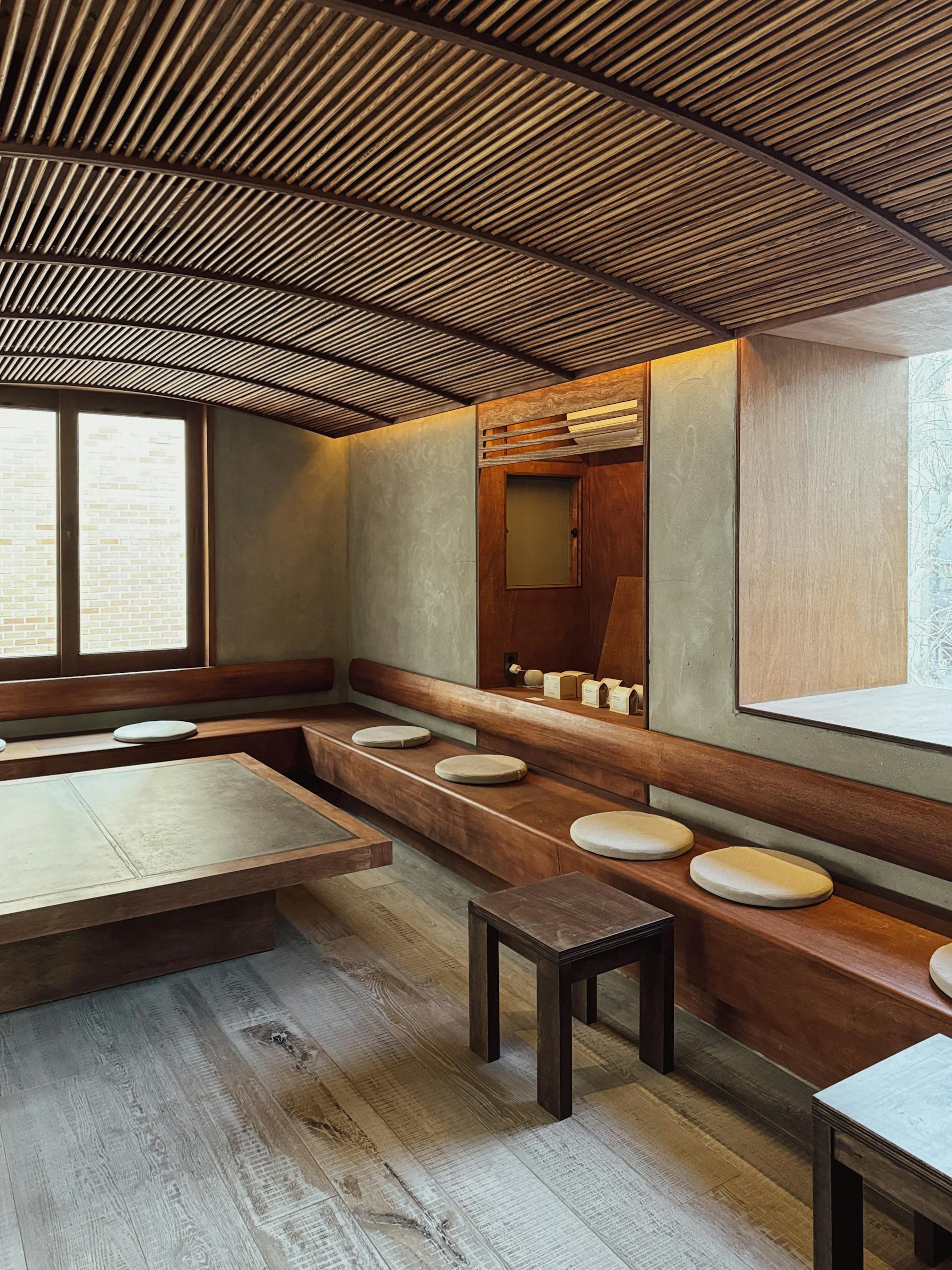 Minimalist interior of a serene room featuring wooden seating, a low table, and large windows allowing natural light.
