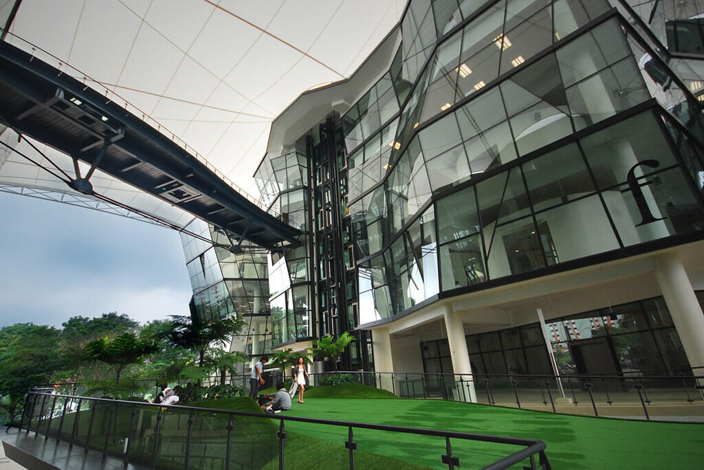 Modern glass-fronted building of LaSalle College with angular architecture, a canopy roof, and green turf landscaping where students are gathered outside.
