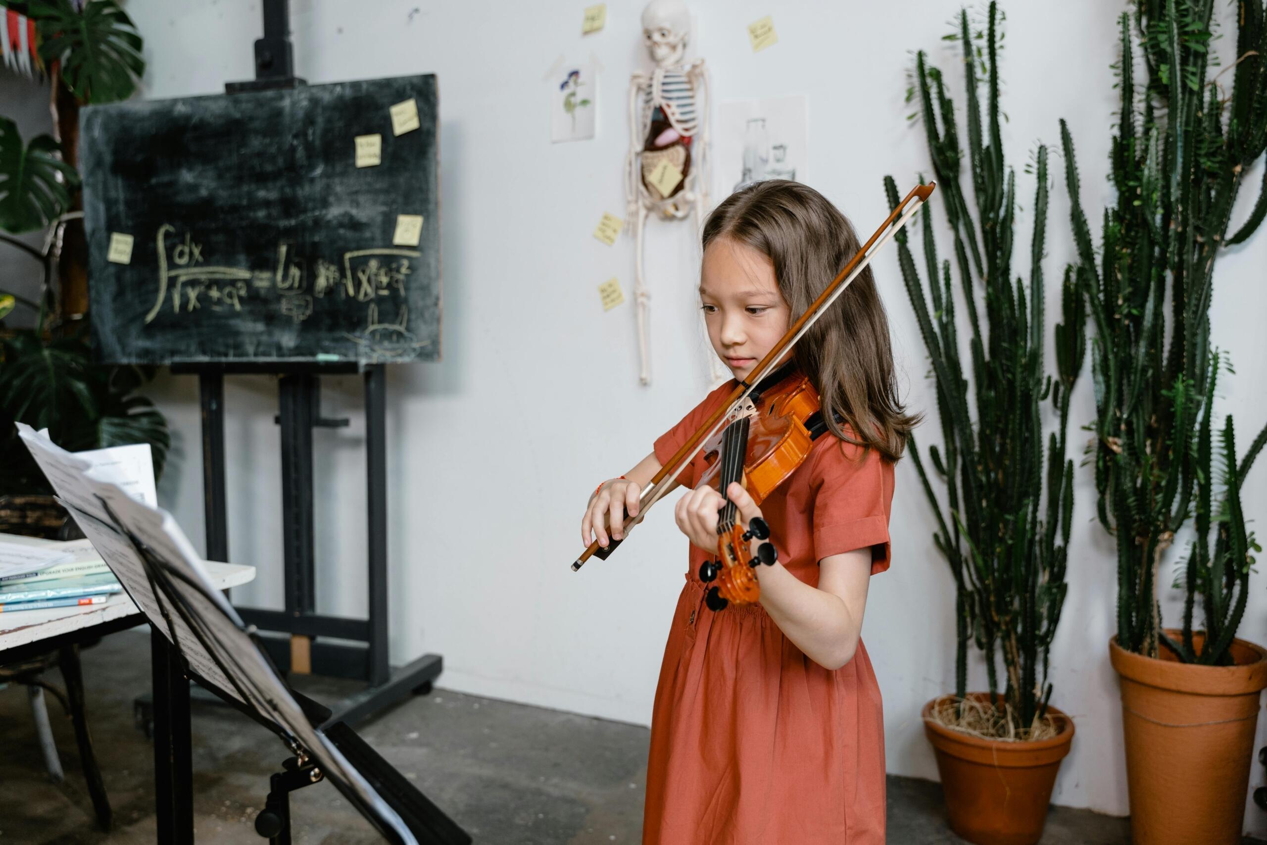 A young student in a red dress plays a violin, standing in front of a chalkboard with mathematical equations and a skeleton model.