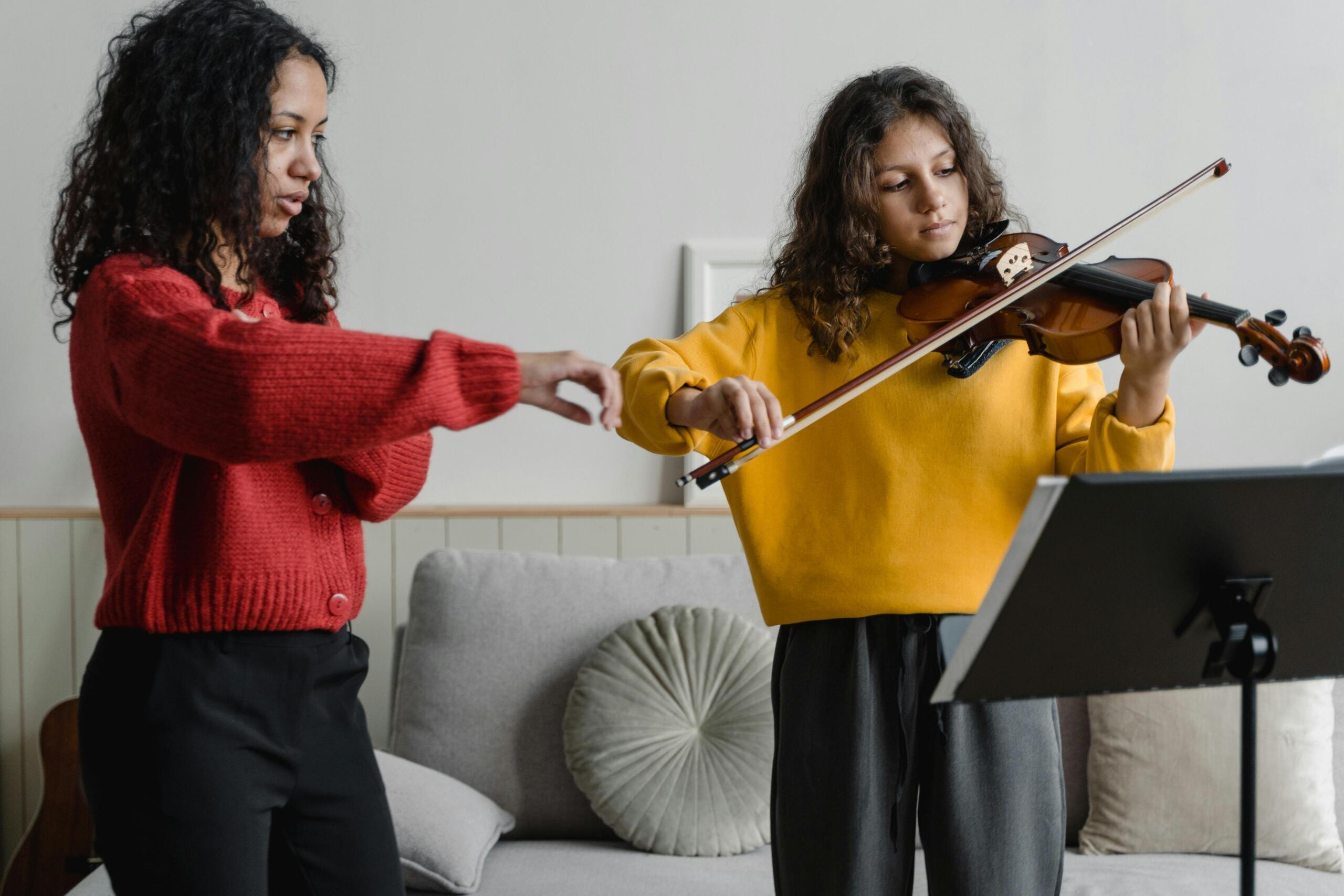 A girl plays the violin while her teacher guides her.
