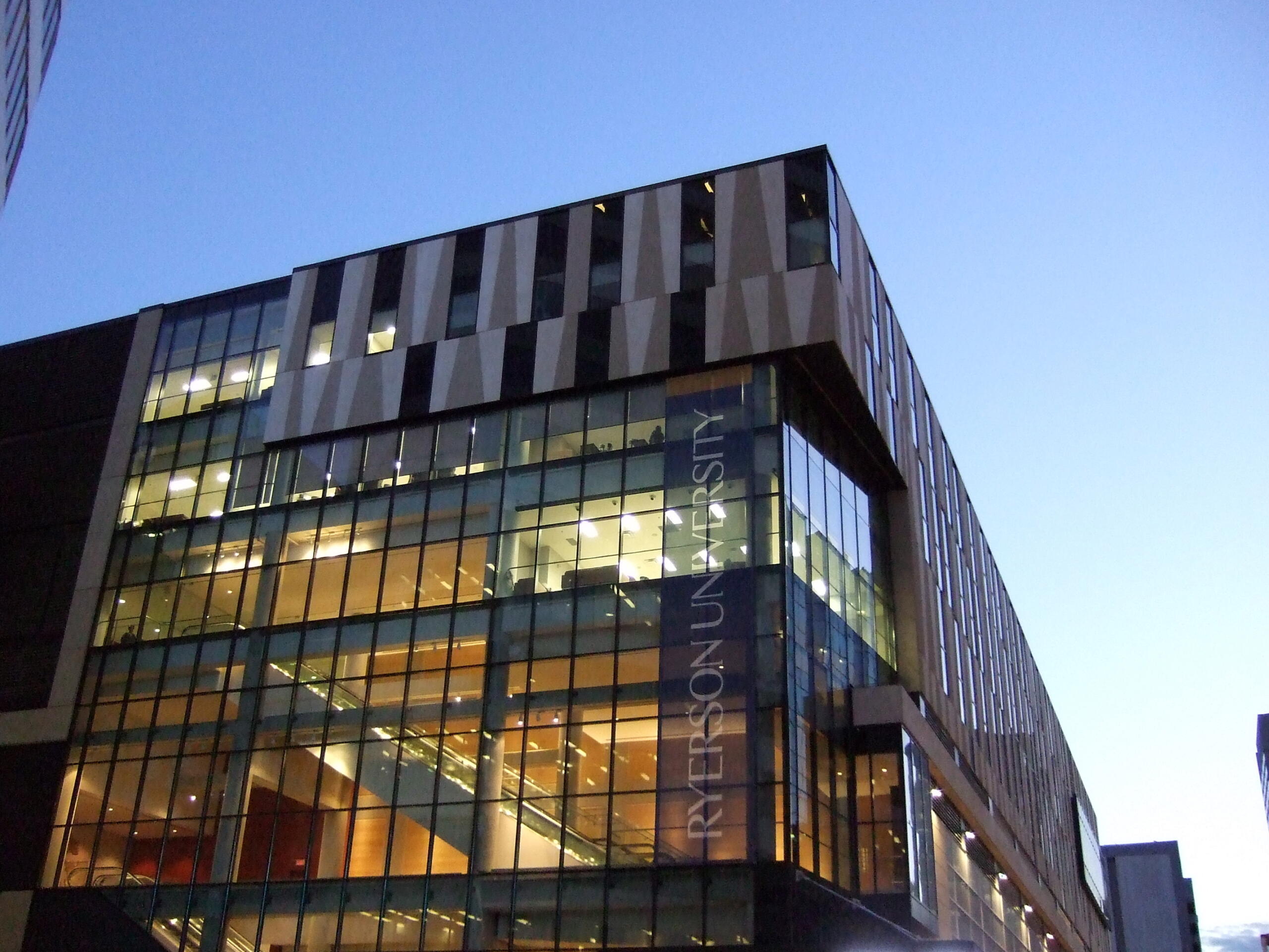 Exterior view of Ryerson University (now Toronto Metropolitan University) building at dusk, with large glass windows and illuminated interior.