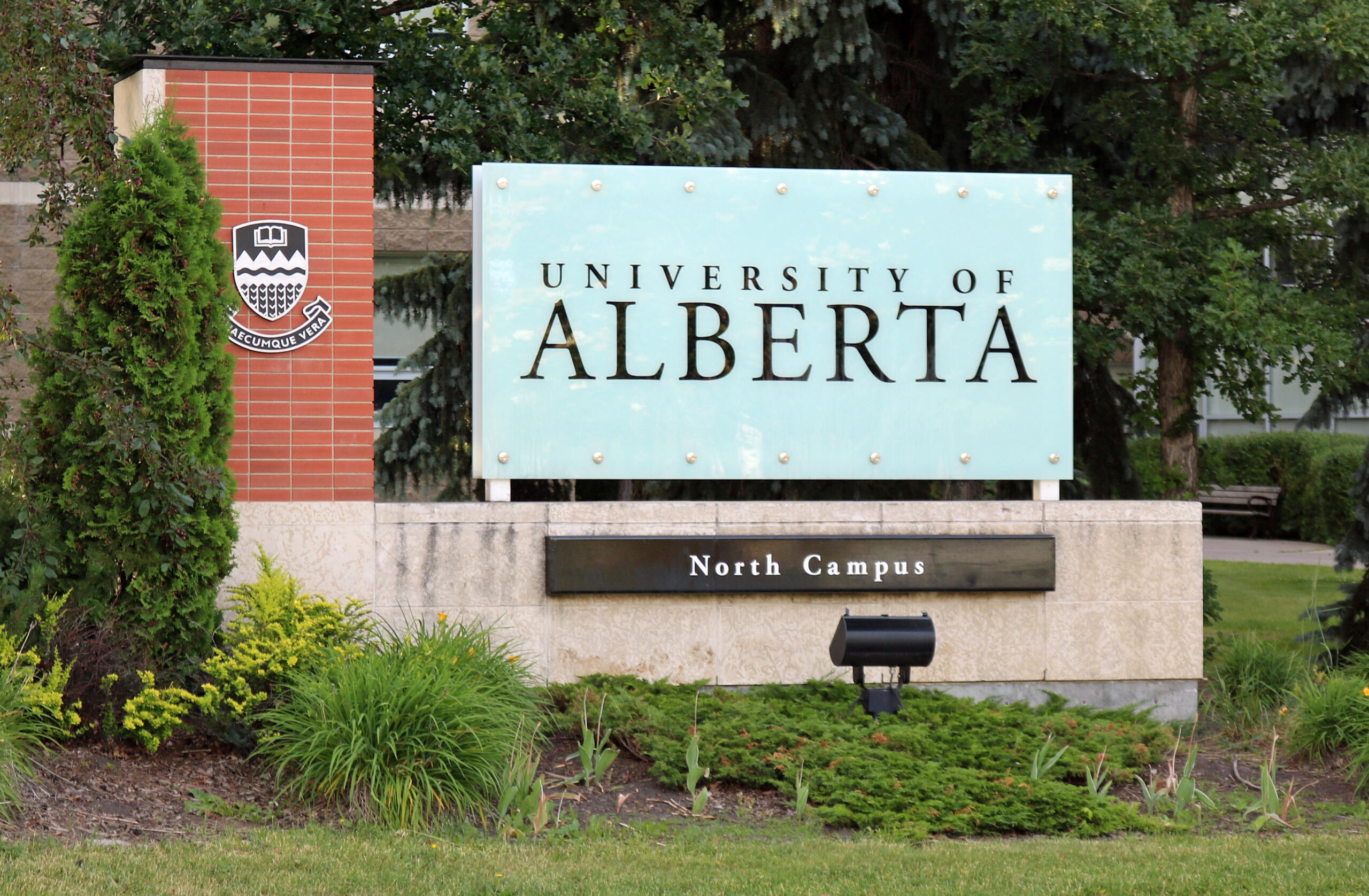 Entrance sign for the University of Alberta North Campus, with surrounding trees, shrubs, and a red brick pillar