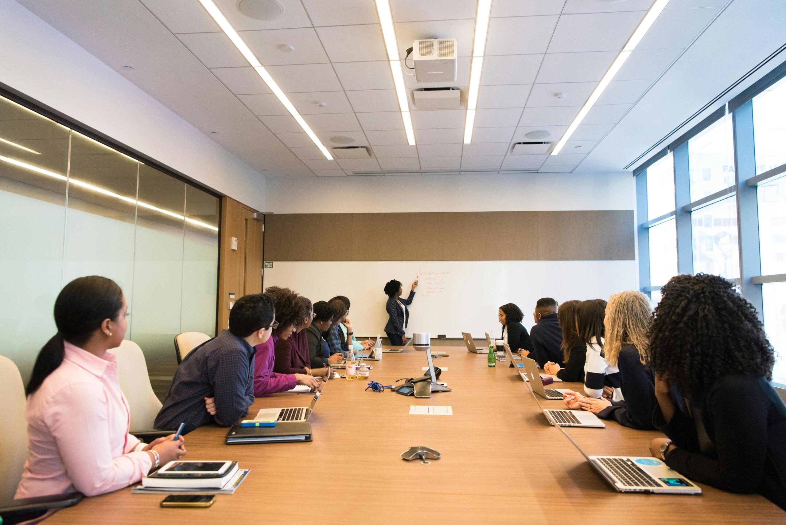 A group of professionals gathered around a conference table during a business board meeting, watching a presentation.