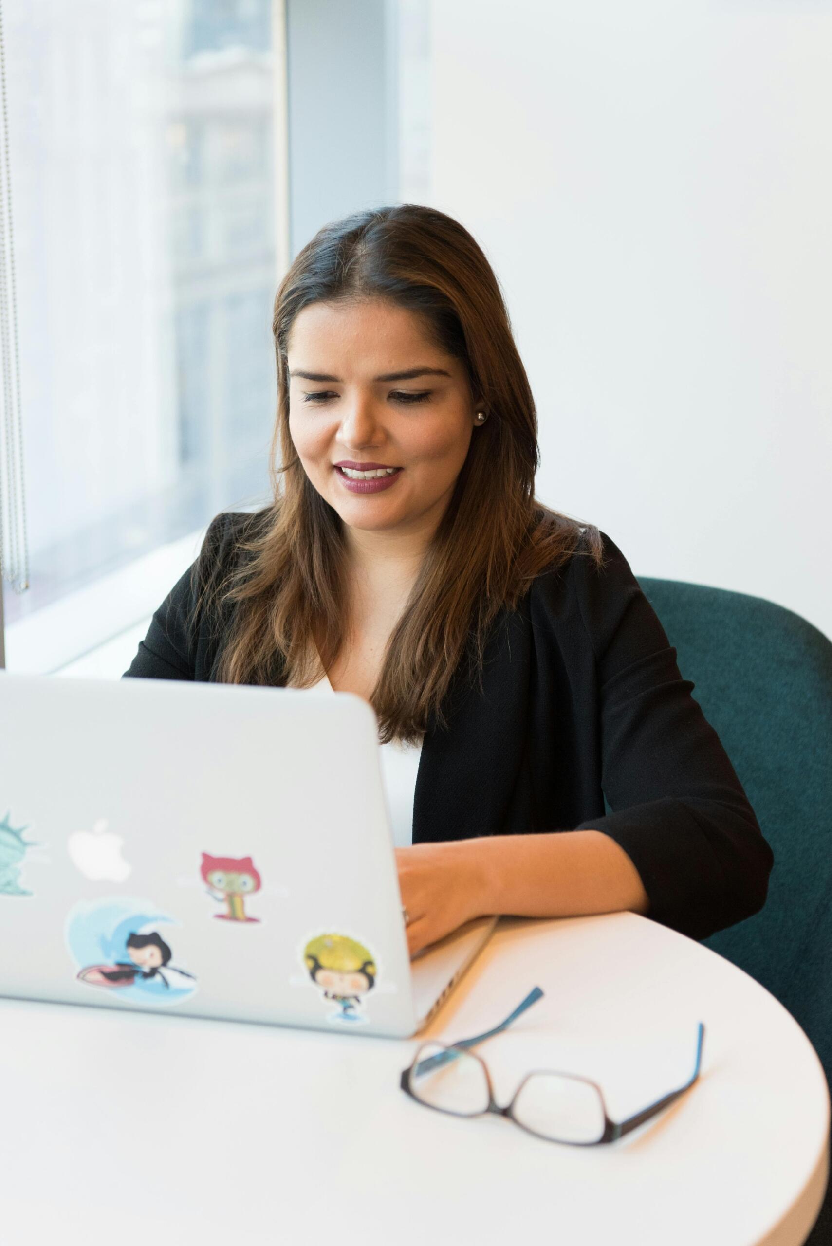 A woman working at her laptop, focused on the screen in a well-lit workspace. Source: Christina Morillo.