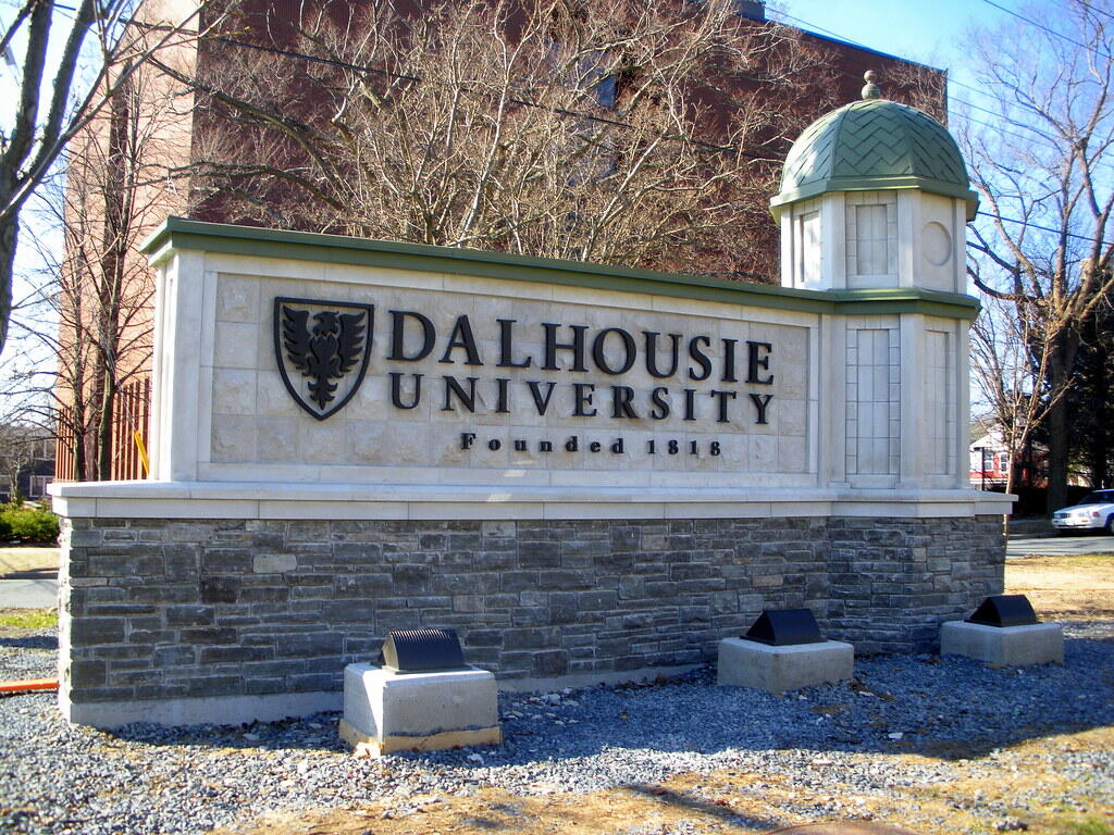 Stone entrance sign of Dalhousie University in Nova Scotia, surrounded by trees and buildings on a clear day.
