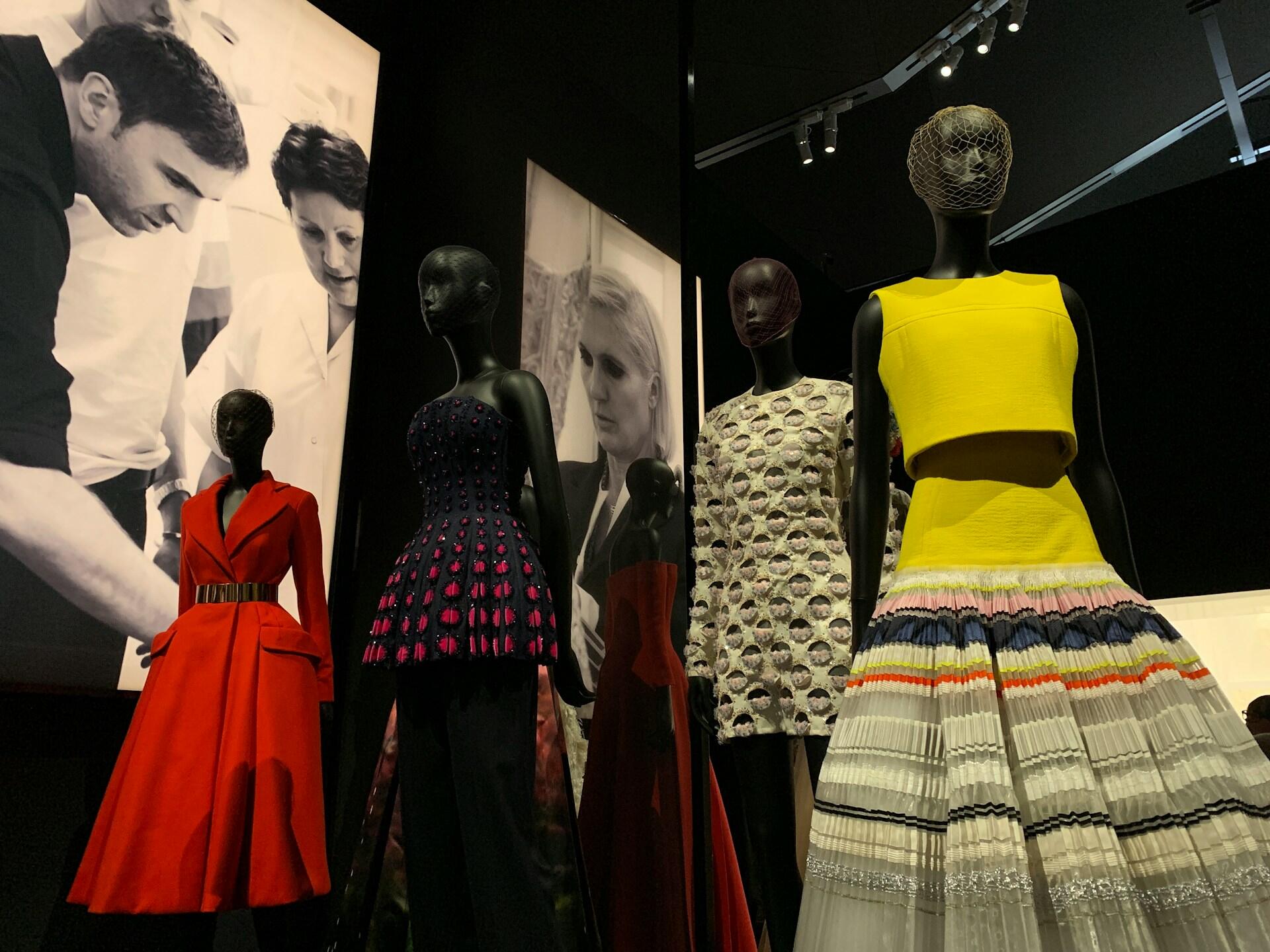 Three stylish mannequins display vibrant fashion pieces: a red dress, a purple peplum top, and a yellow crop top paired with a multi-striped skirt.