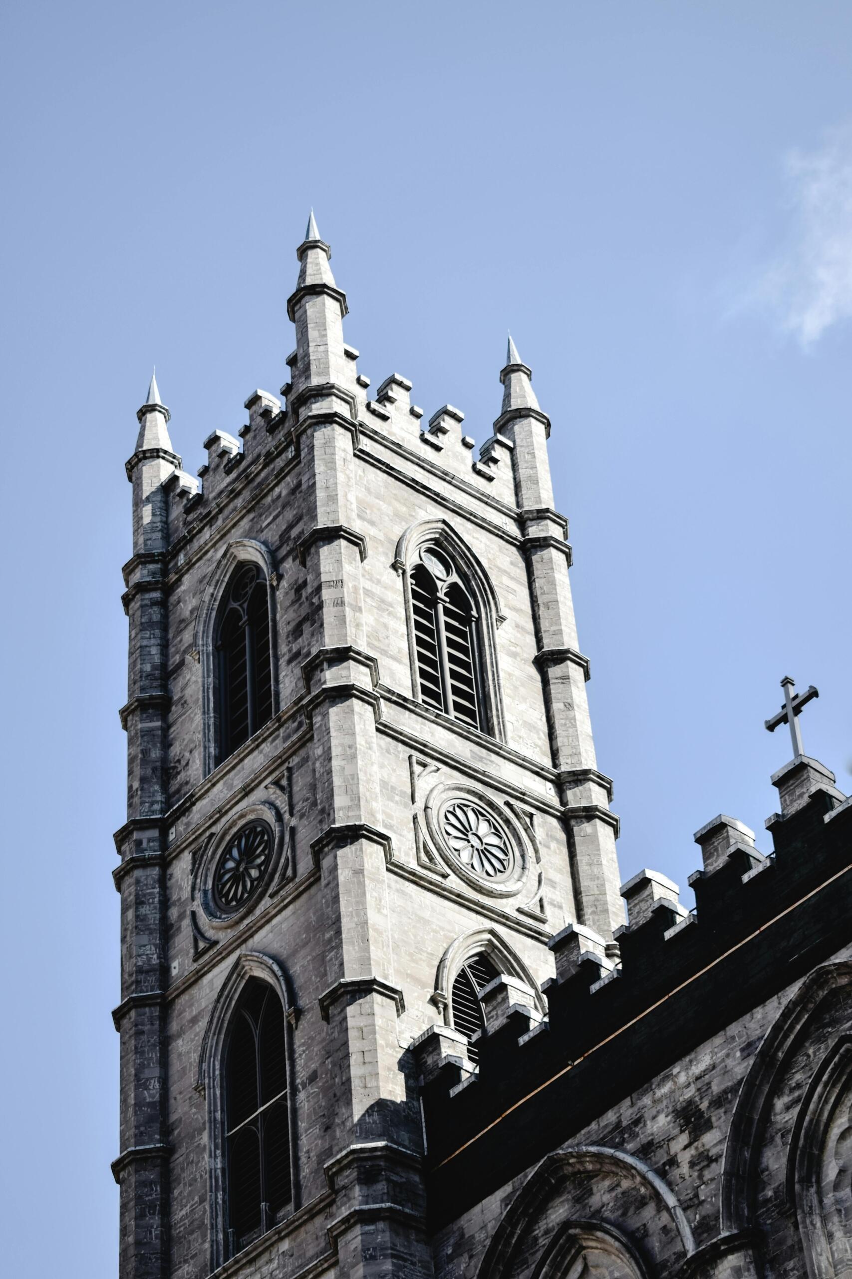 A historic church clock tower in Old Montreal, with detailed stonework and a large clock face set against a bright blue sky.