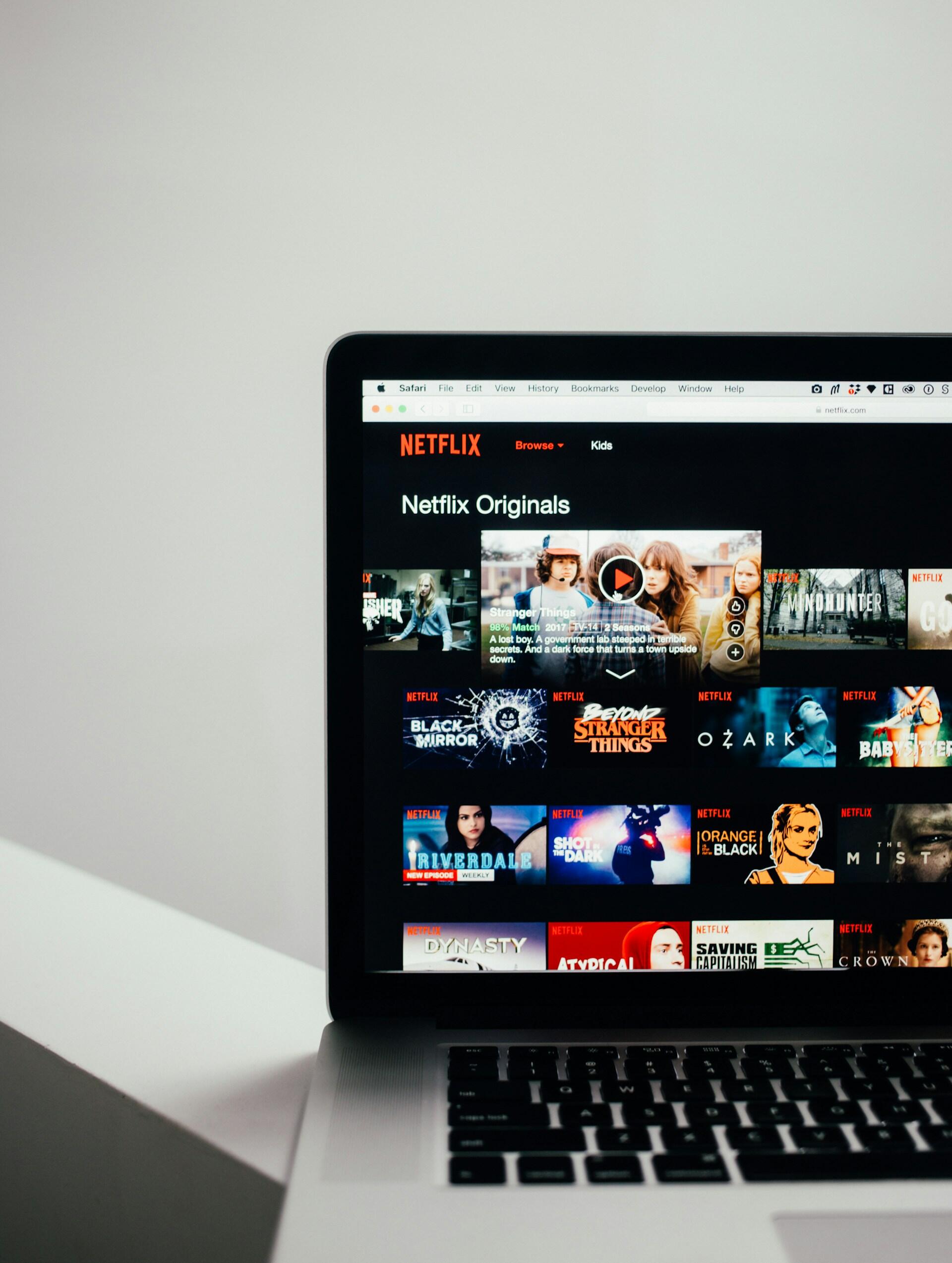 A laptop screen displaying the Netflix homepage, featuring various Netflix Originals thumbnails against a dark background.
