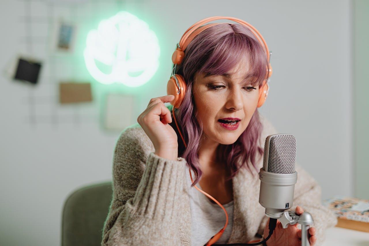A person wearing orange headphones sits in front of a microphone, with a green glowing plant sign in the background.