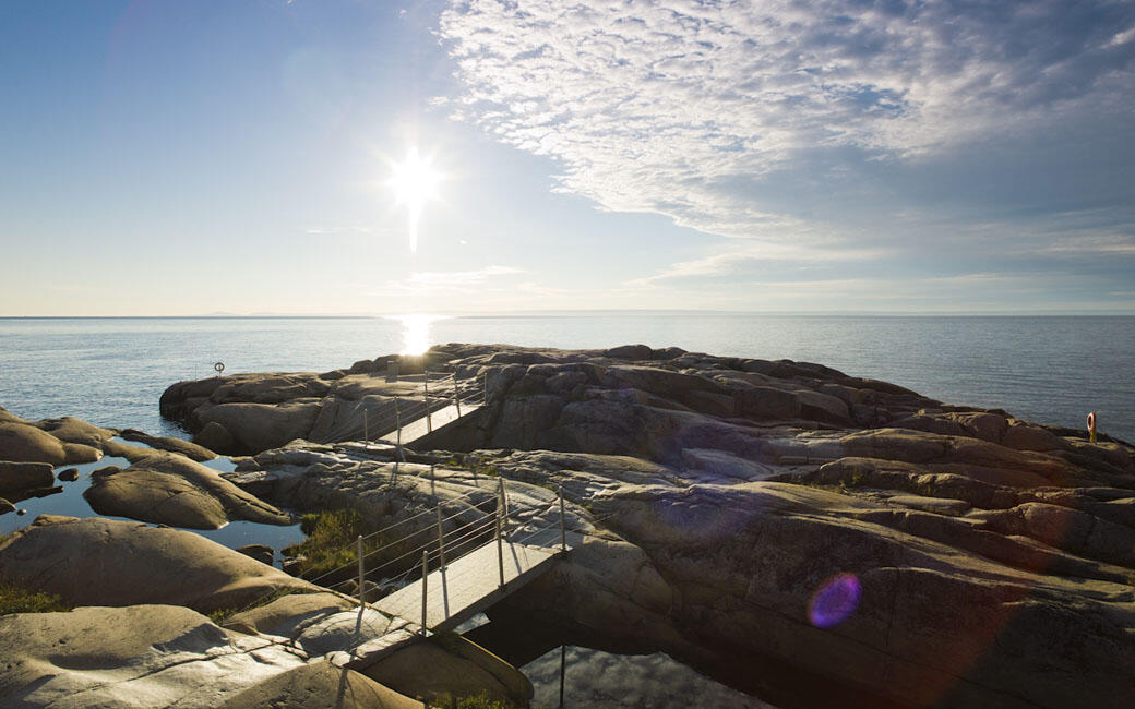 Rocky coastal shoreline with metal walkways and sun reflecting off calm ocean water along the Canadian coastline in Quebec.