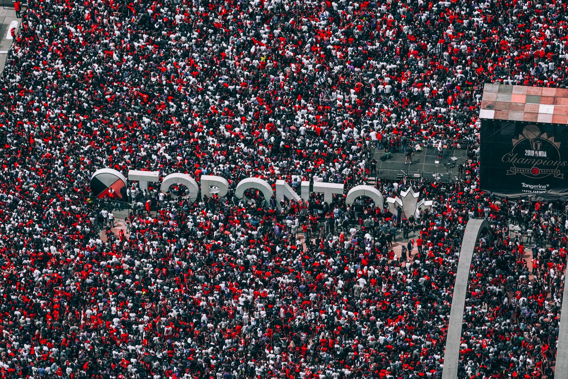 Aerial view of a massive crowd in Toronto, predominantly wearing red, celebrating an event near the iconic "TORONTO" sign.