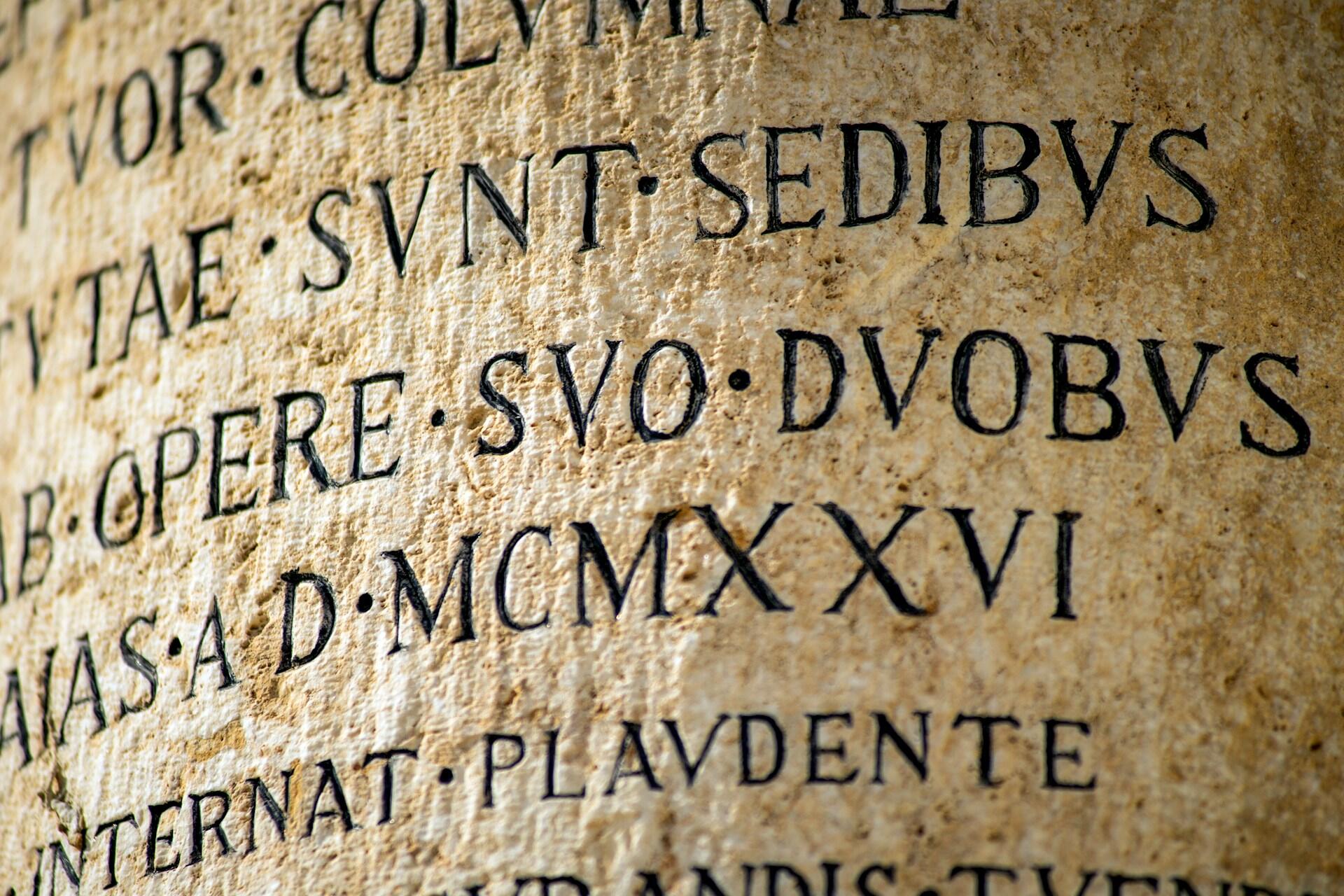Close-up of an ancient stone inscription featuring Latin text and Roman numerals, revealing historical and cultural significance.