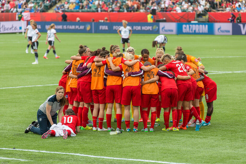 The Canadian women’s soccer team gathers in a pre-game huddle on the field during the 2015 FIFA Women’s World Cup in Canada, showcasing team unity and focus.