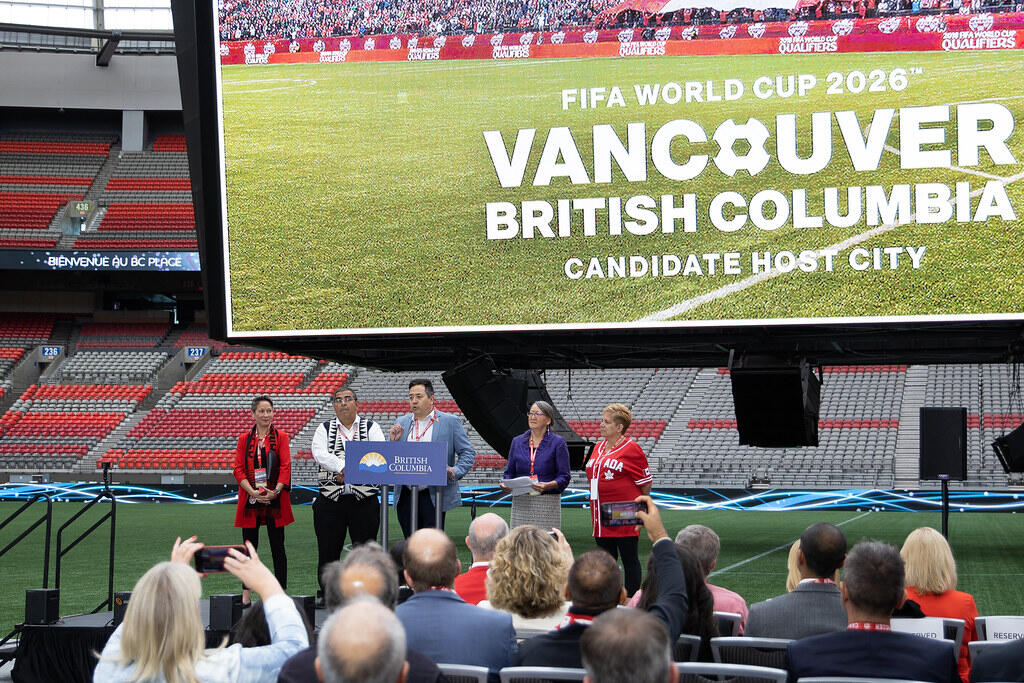 Officials and community leaders speak at BC Place Stadium in front of a large screen announcing Vancouver, British Columbia as a candidate host city for the FIFA World Cup 2026.