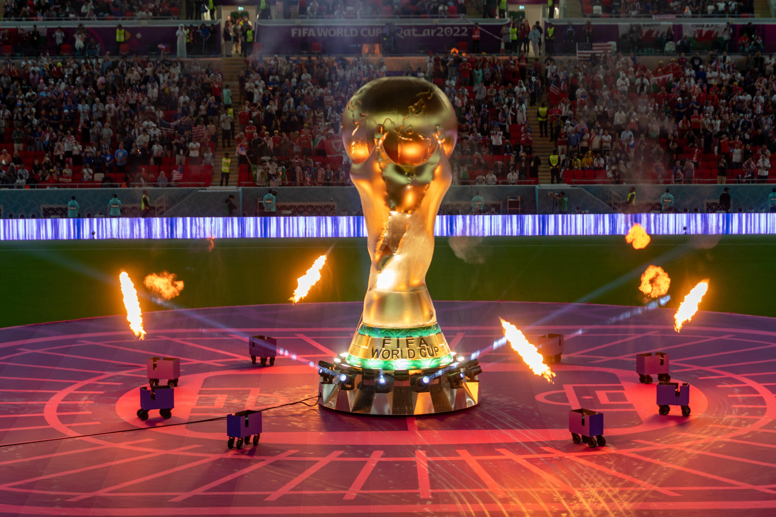 FIFA World Cup trophy on display with flames and lights during the opening ceremony in a packed stadium.