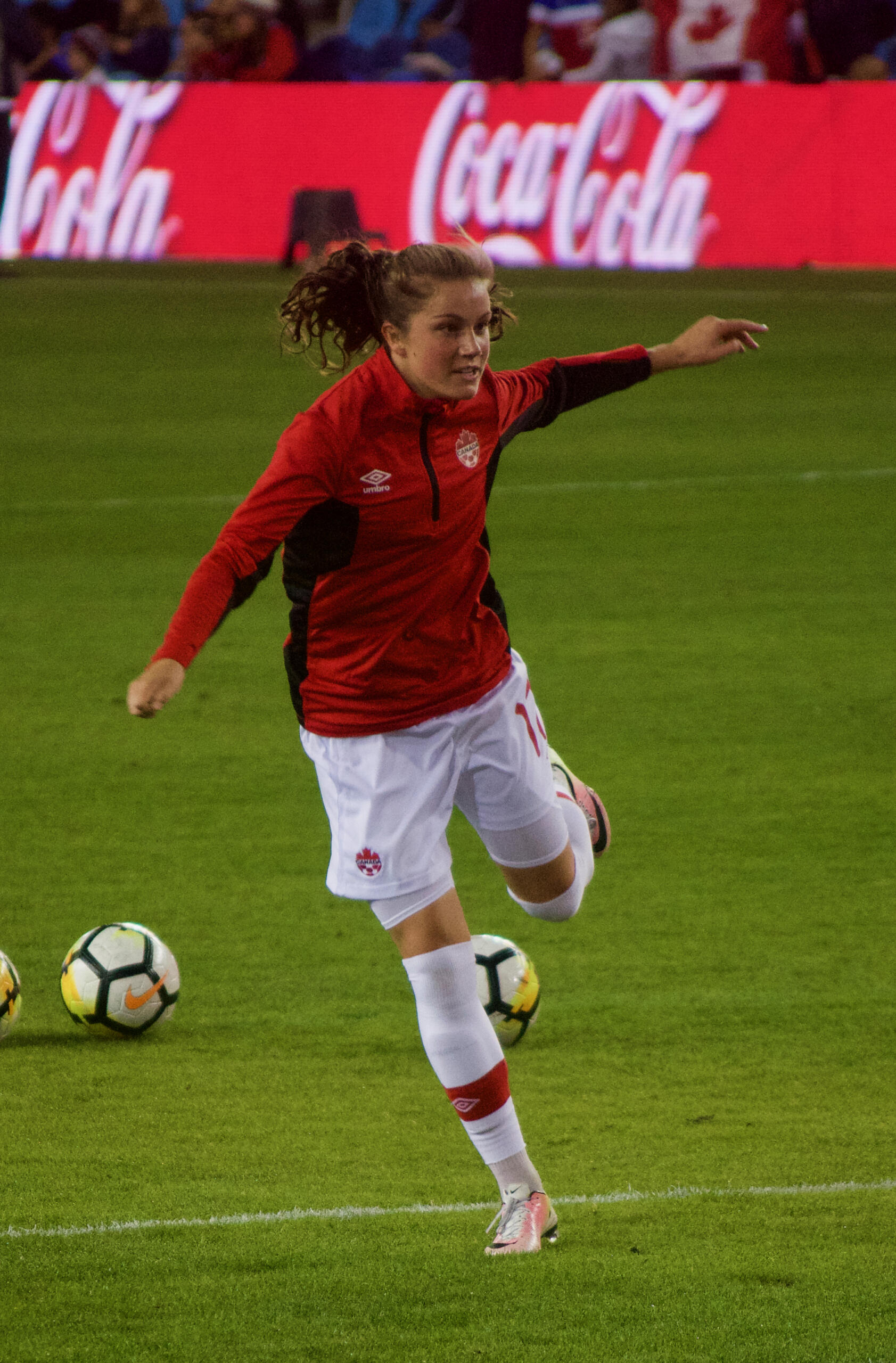 Jessie Fleming in a red Canada training top, kicking a ball during warm-up before an international match.