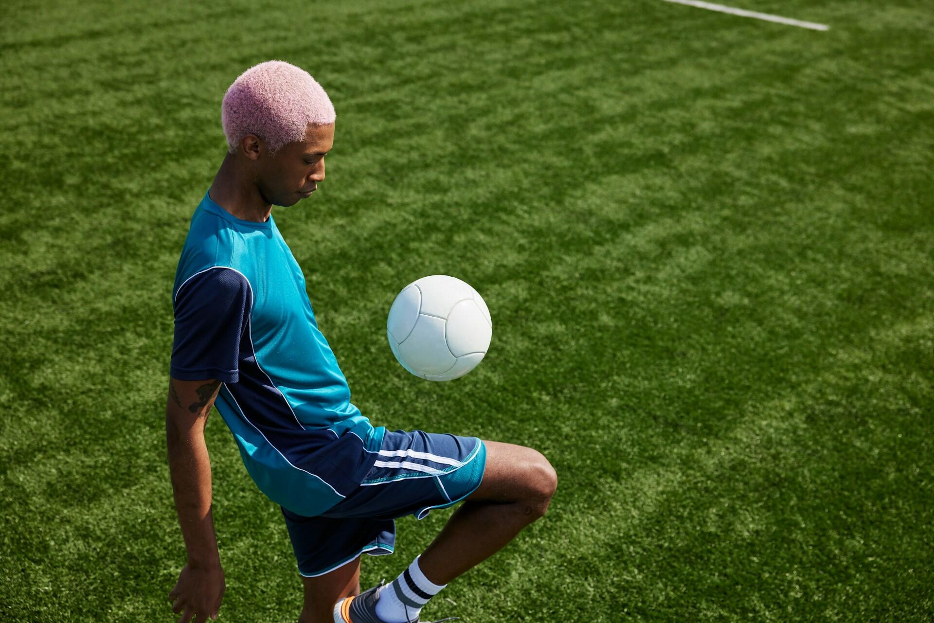 A person in a blue sports outfit skillfully balances a soccer ball on their knee on a green artificial turf field.