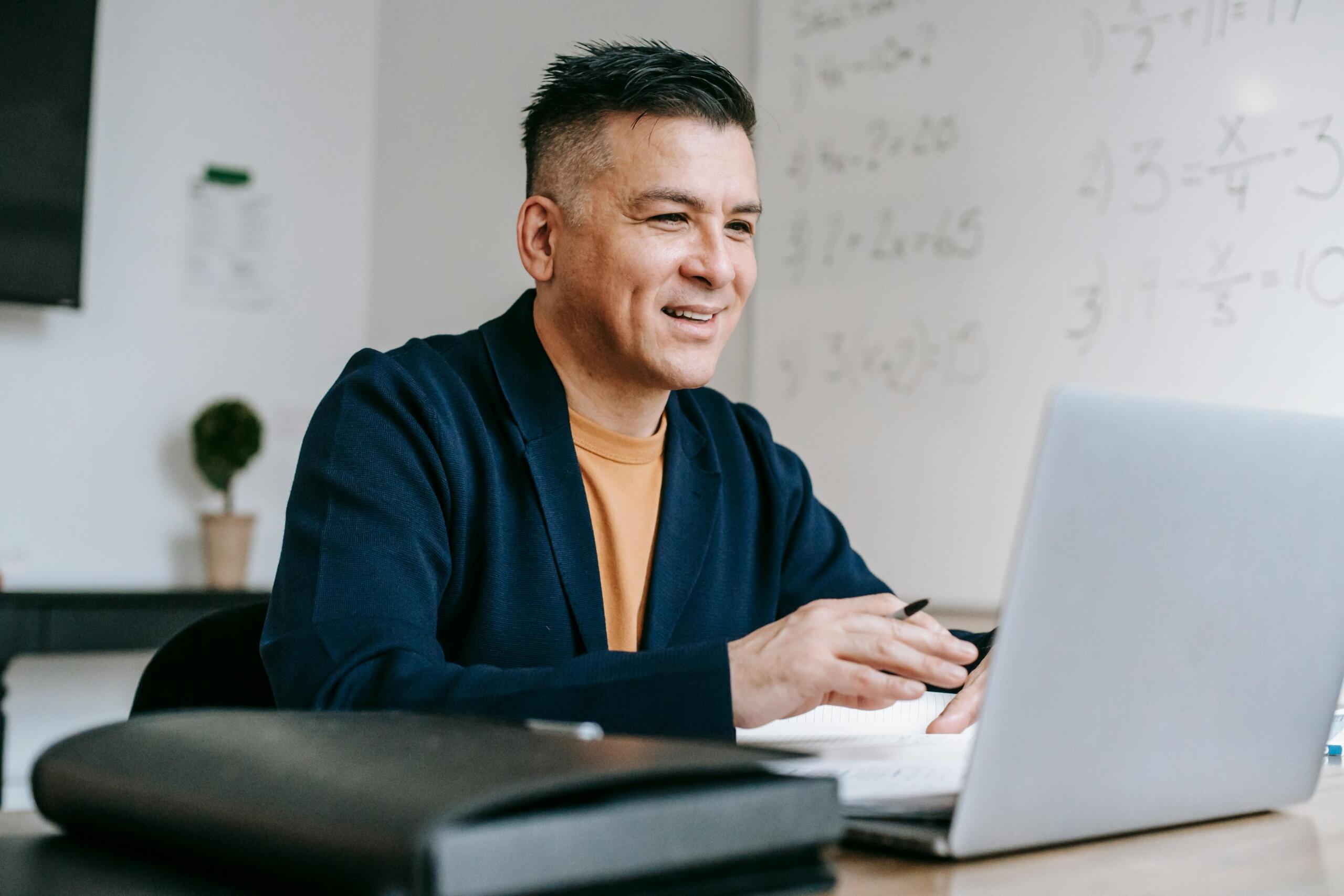 A male professional sitting at a desk, attentively looking at a laptop screen, appearing focused and engaged with his work.