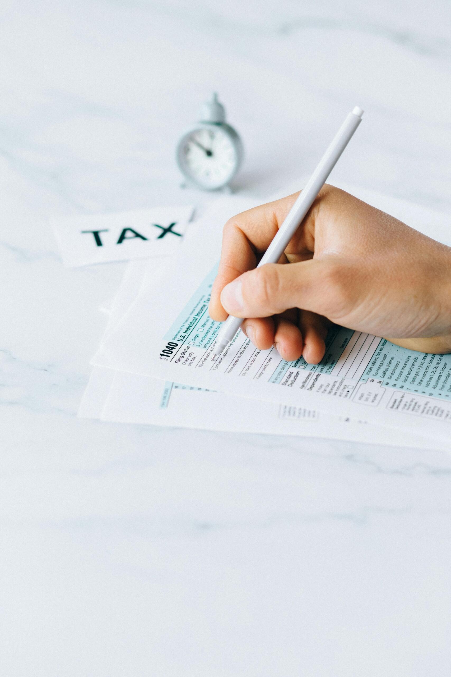 A person filling out a tax form at a desk, holding a pen and reviewing financial documents.