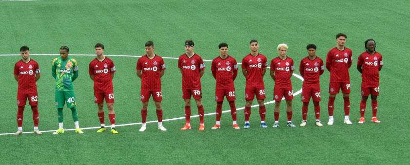 Toronto FC players lined up on the pitch before kickoff, wearing their red home kits during a 2024 MLS Next Pro match.