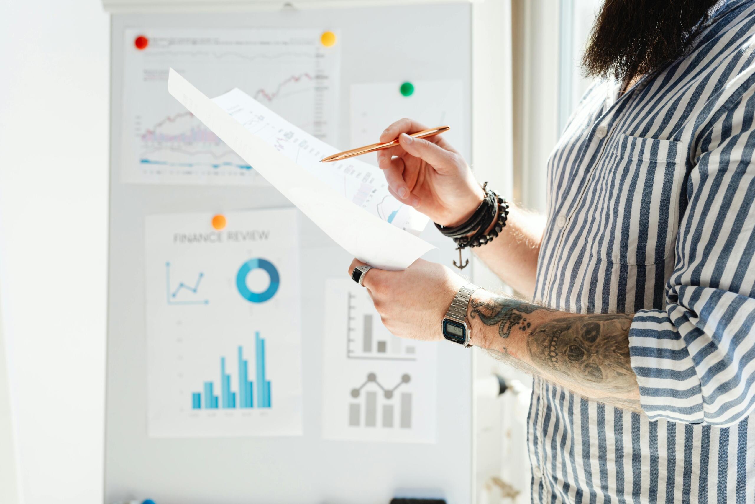 Person reviewing printed data charts in front of a whiteboard with financial graphs and analytics.