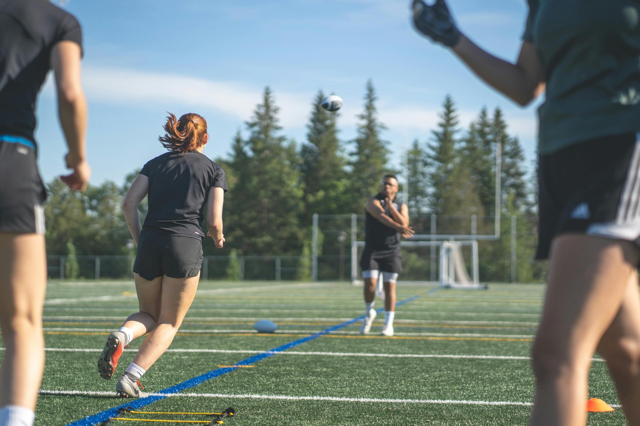 A group of women playing soccer on a grassy field with the sun shining brightly overhead.