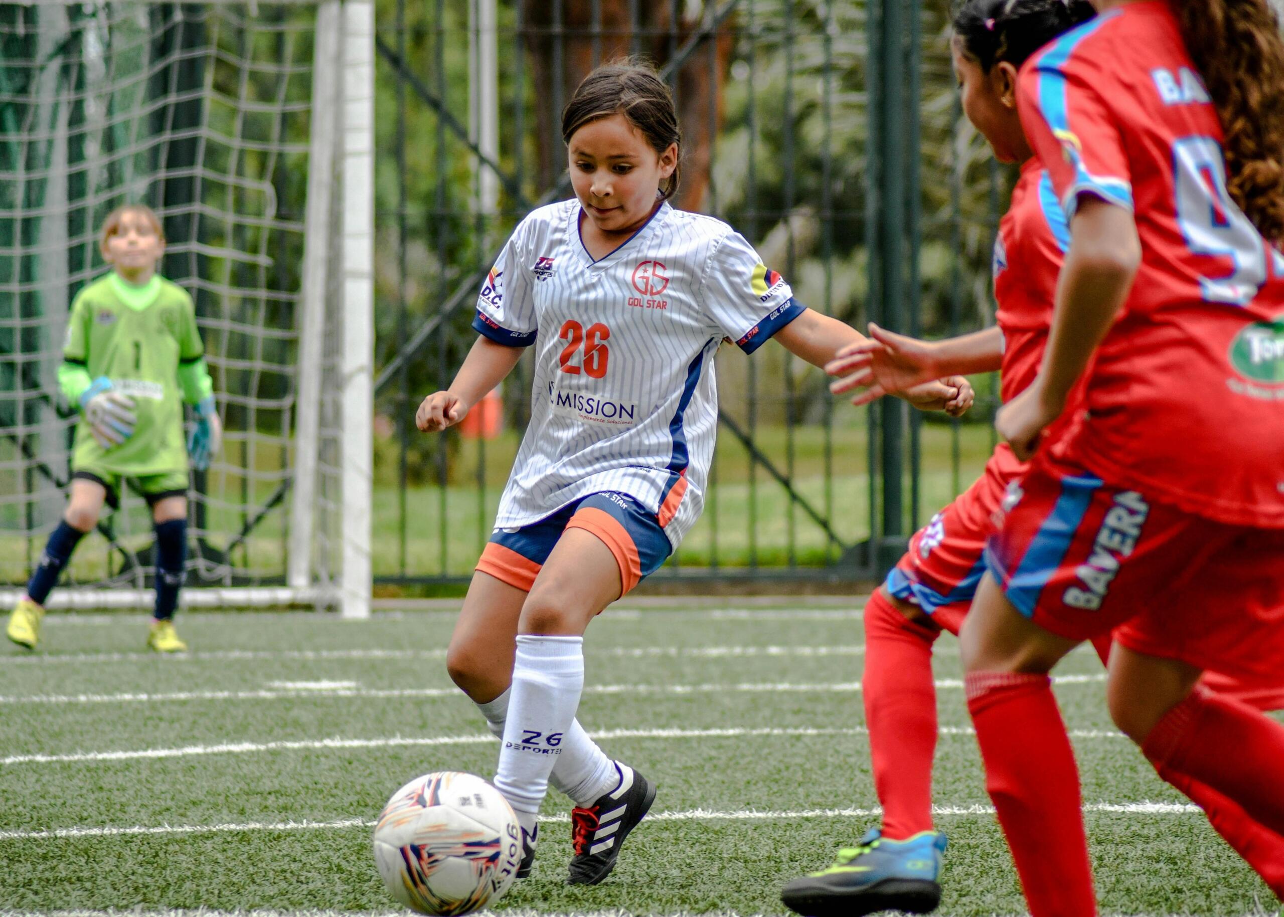 A child dribbling a soccer ball on a field during a game, focused and in motion.