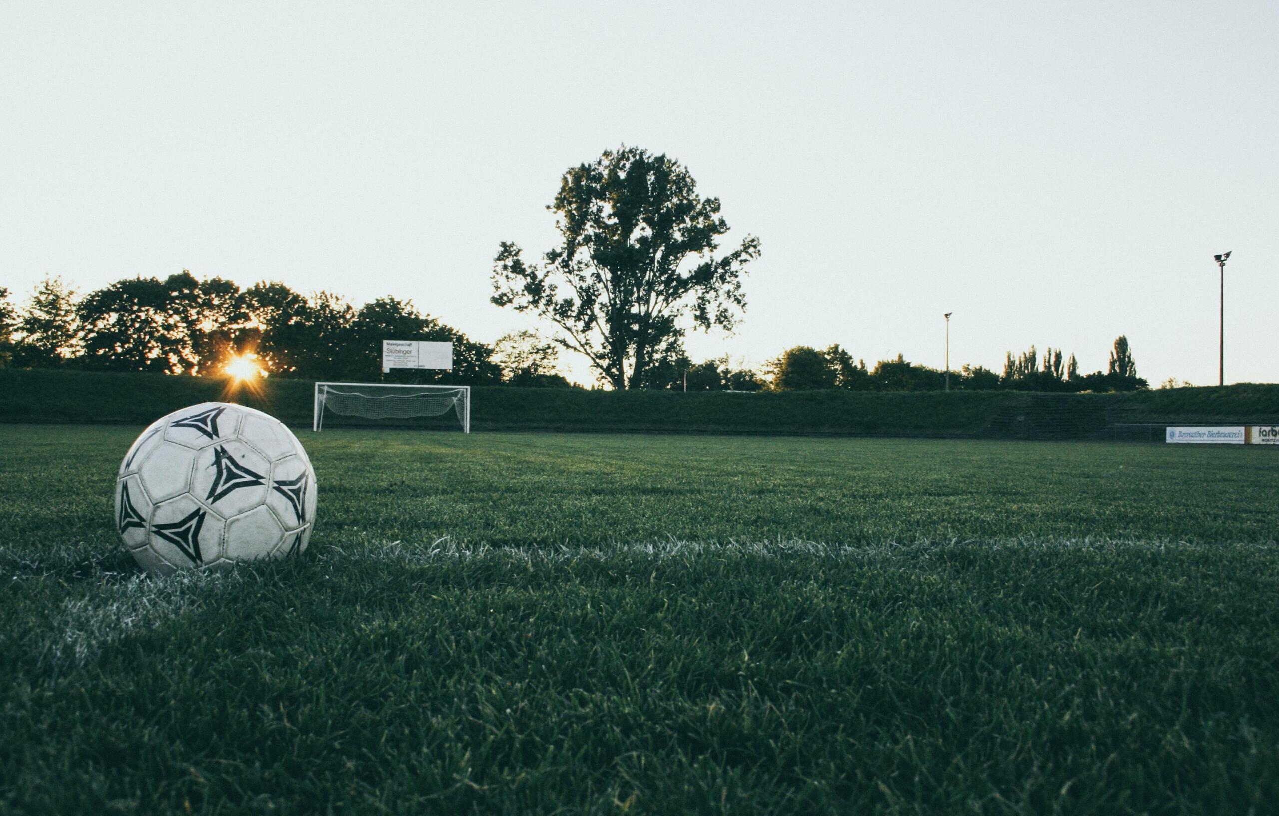A soccer ball resting in the corner of a grass field near the boundary line.