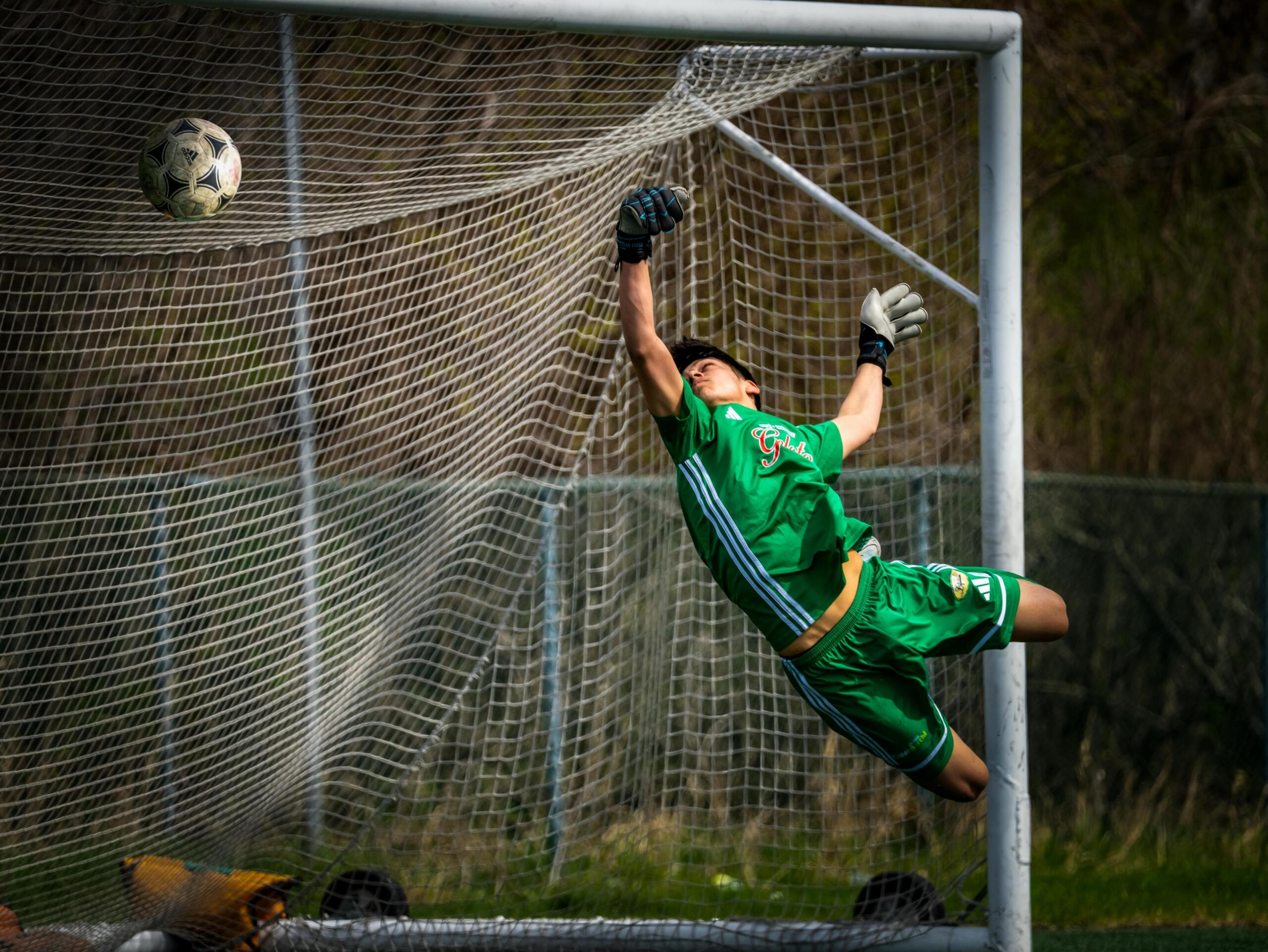 A soccer goalie leaping to block a ball in midair during a game.