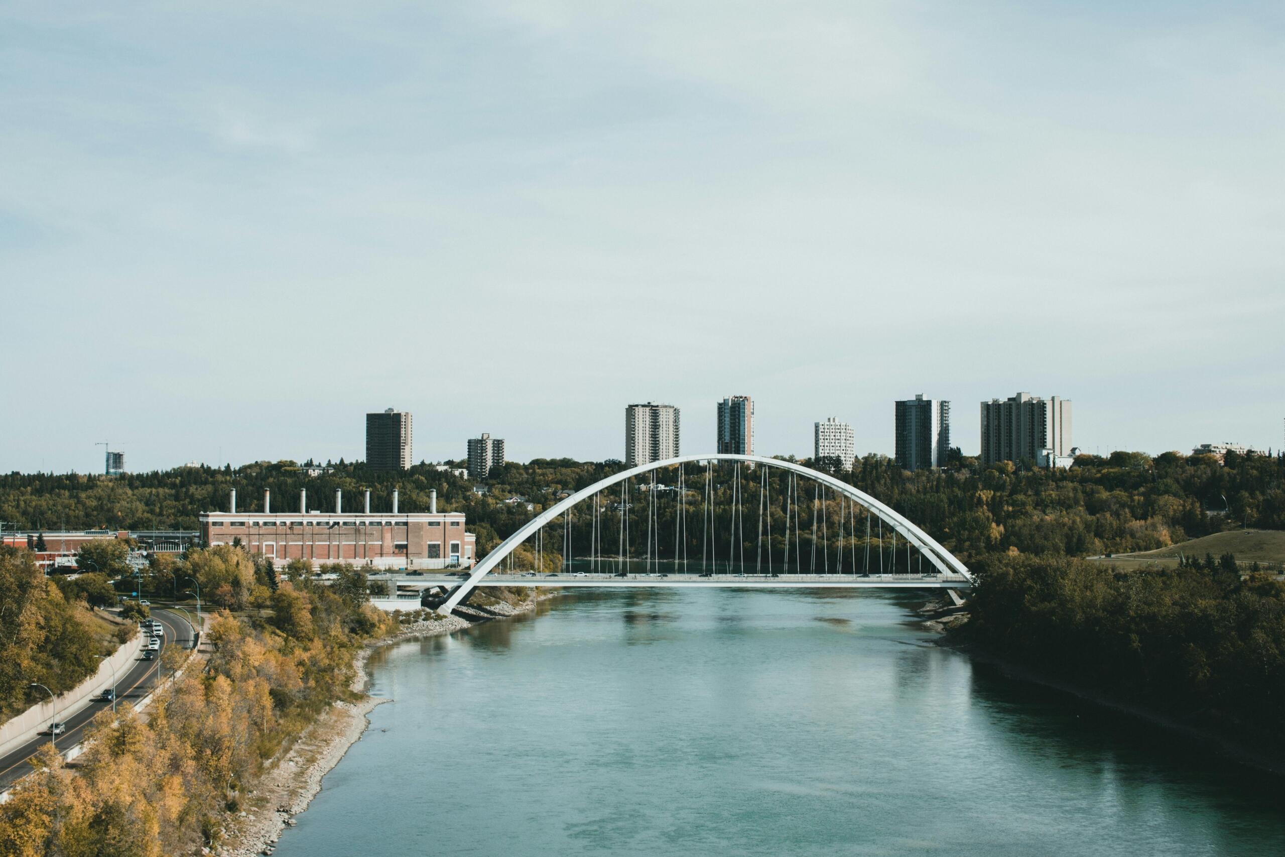 A scenic view of Edmonton featuring a bridge spanning over the North Saskatchewan River, with the city skyline and lush greenery in the background.