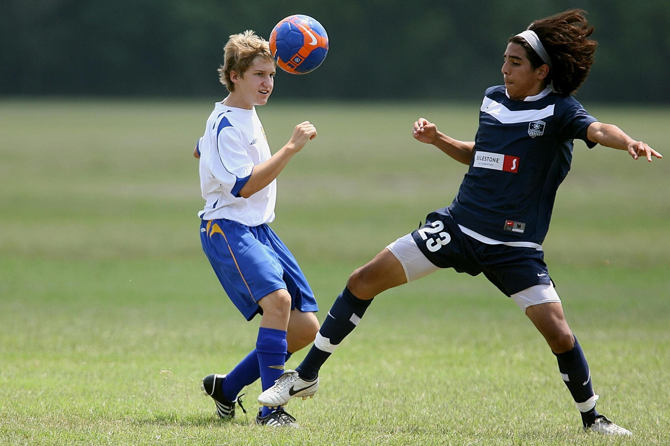Two soccer players competing for control as the ball hovers in mid-air between them, both focused and ready to make their move on the field.