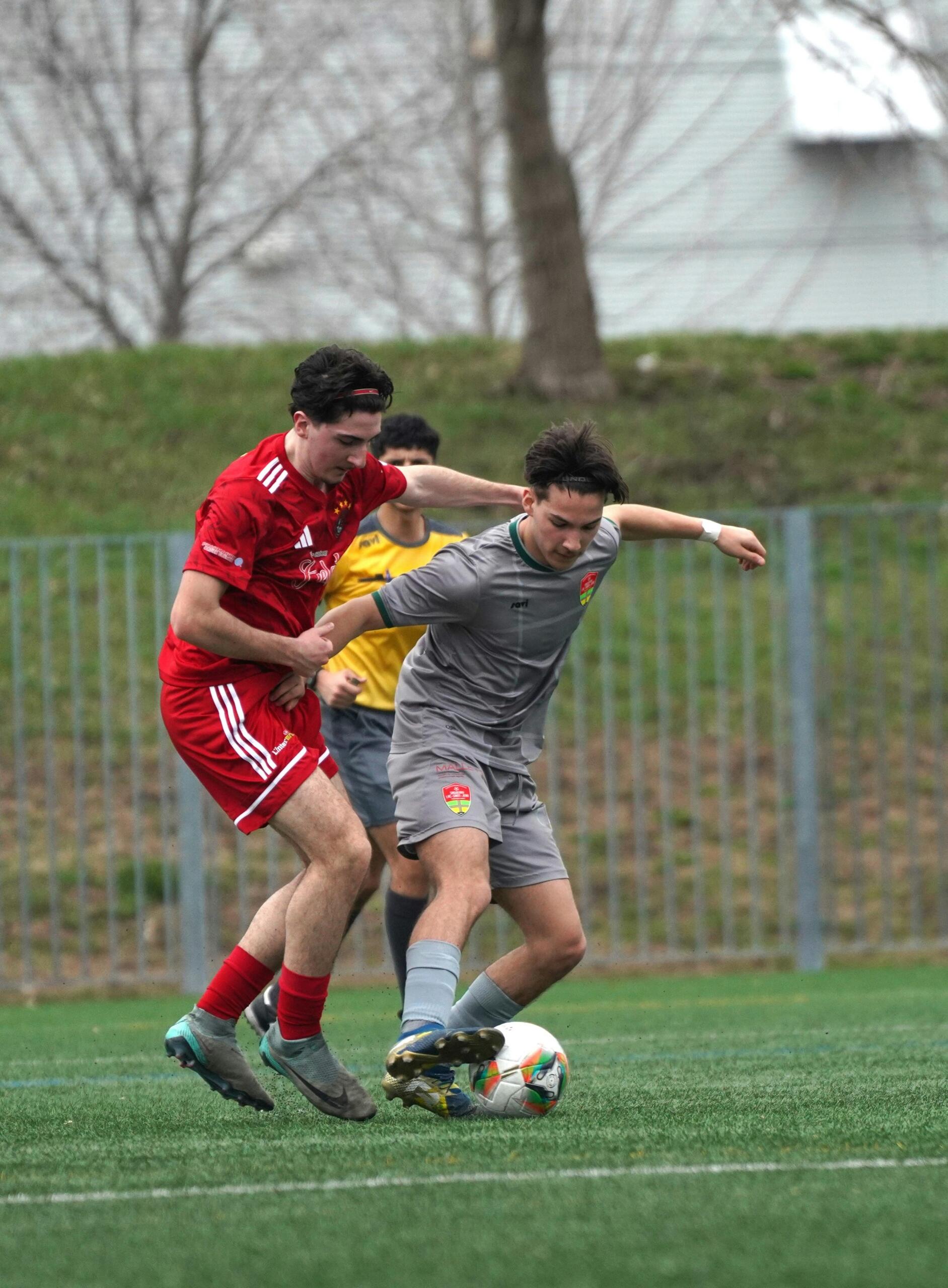 Two male soccer players intensely competing for the ball, both in motion with extended legs and focused expressions during a match on the field.