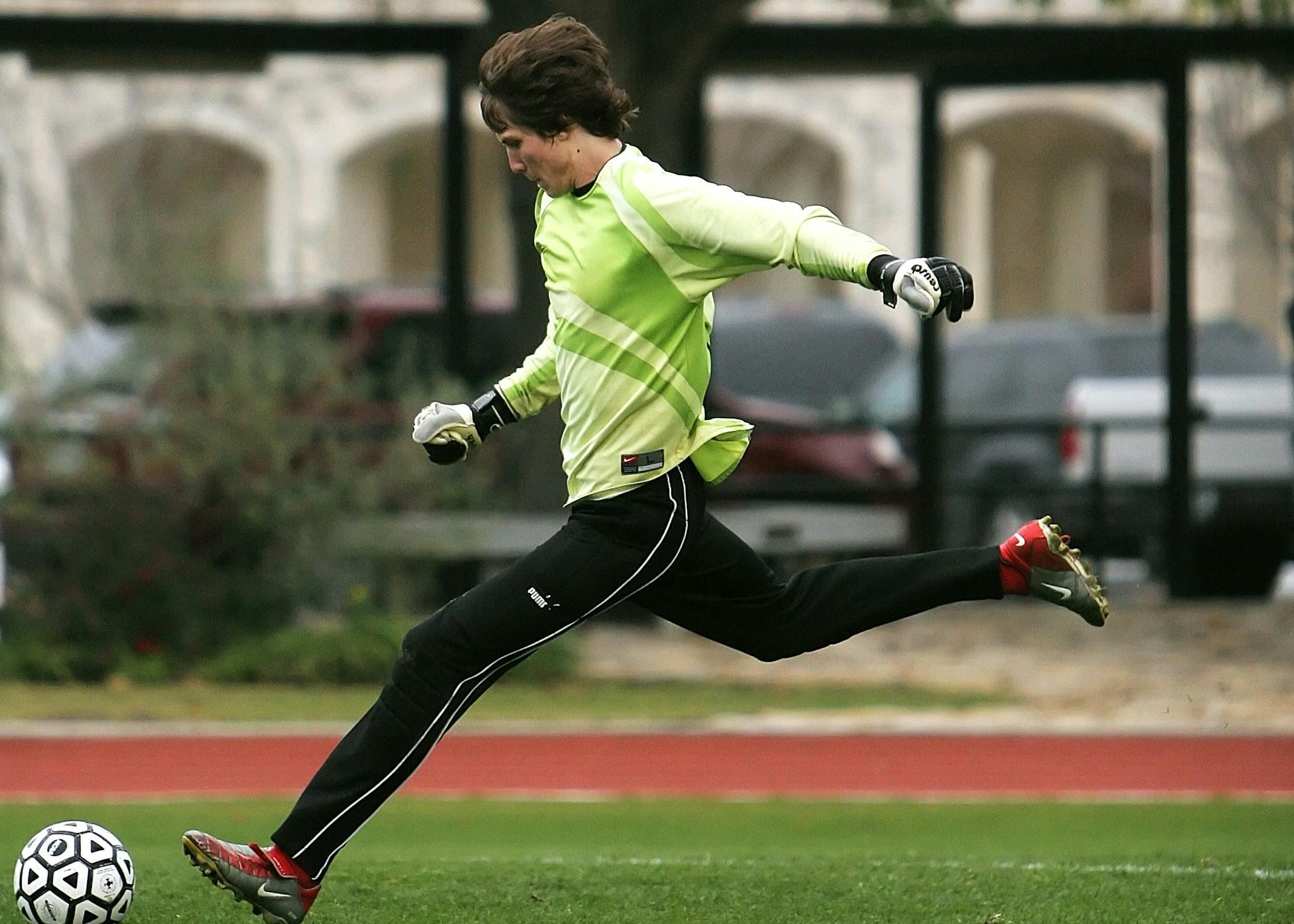  A male soccer player sprinting across a green field, focused and determined, with his eyes on the ball and arms pumping for speed.