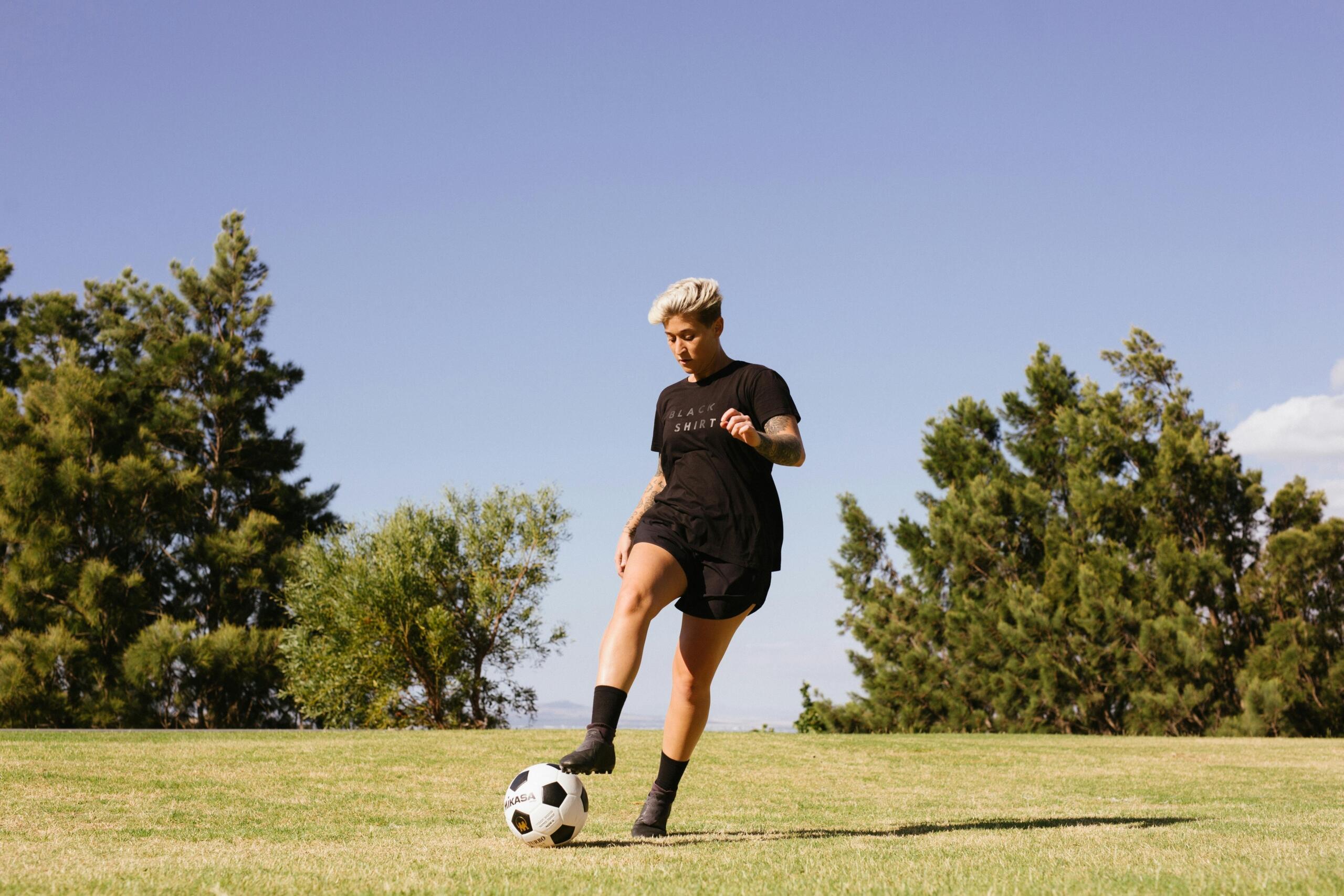 A man in athletic gear kicking a soccer ball on a grassy field, captured mid-motion with one leg extended kicking a ball.