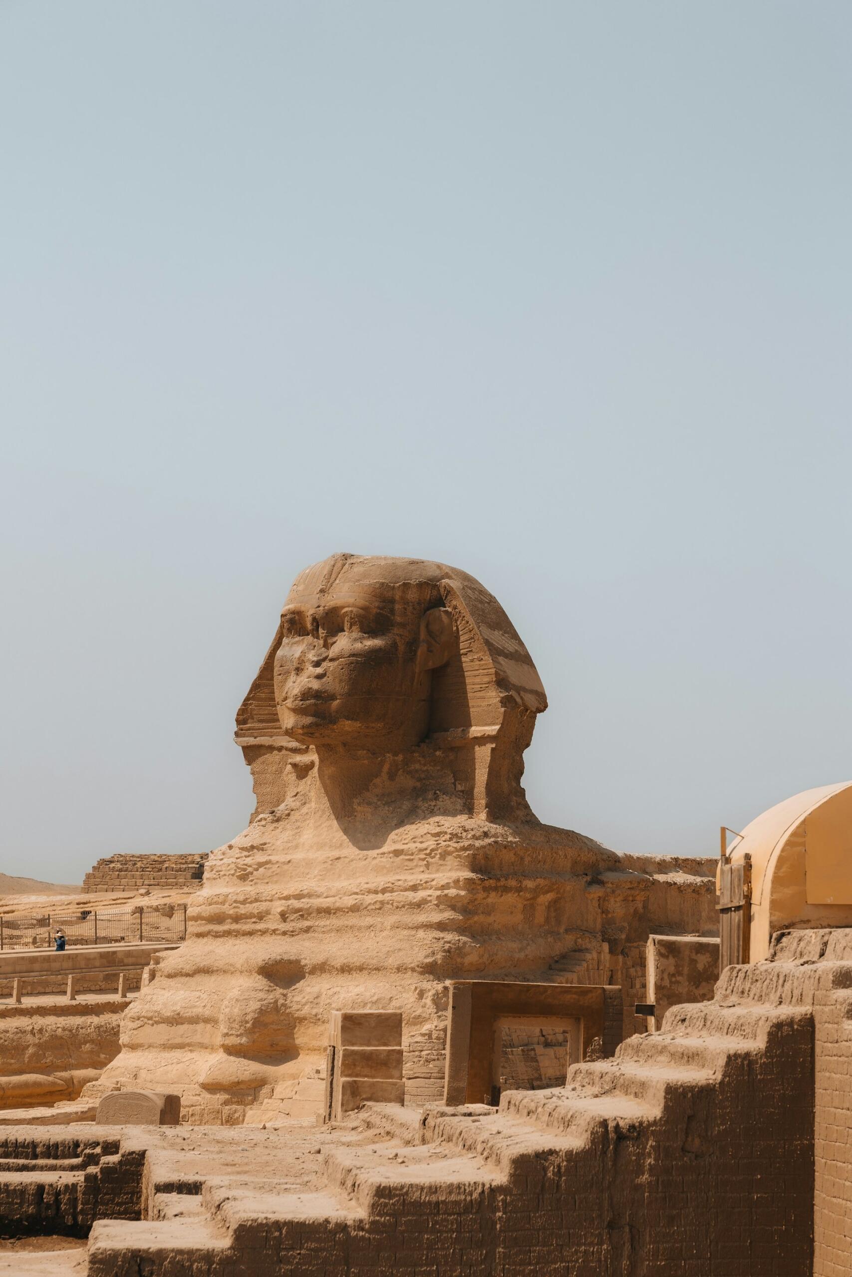 The Great Sphinx of Giza, a massive limestone statue with a lion's body and a human head, against a clear blue sky.