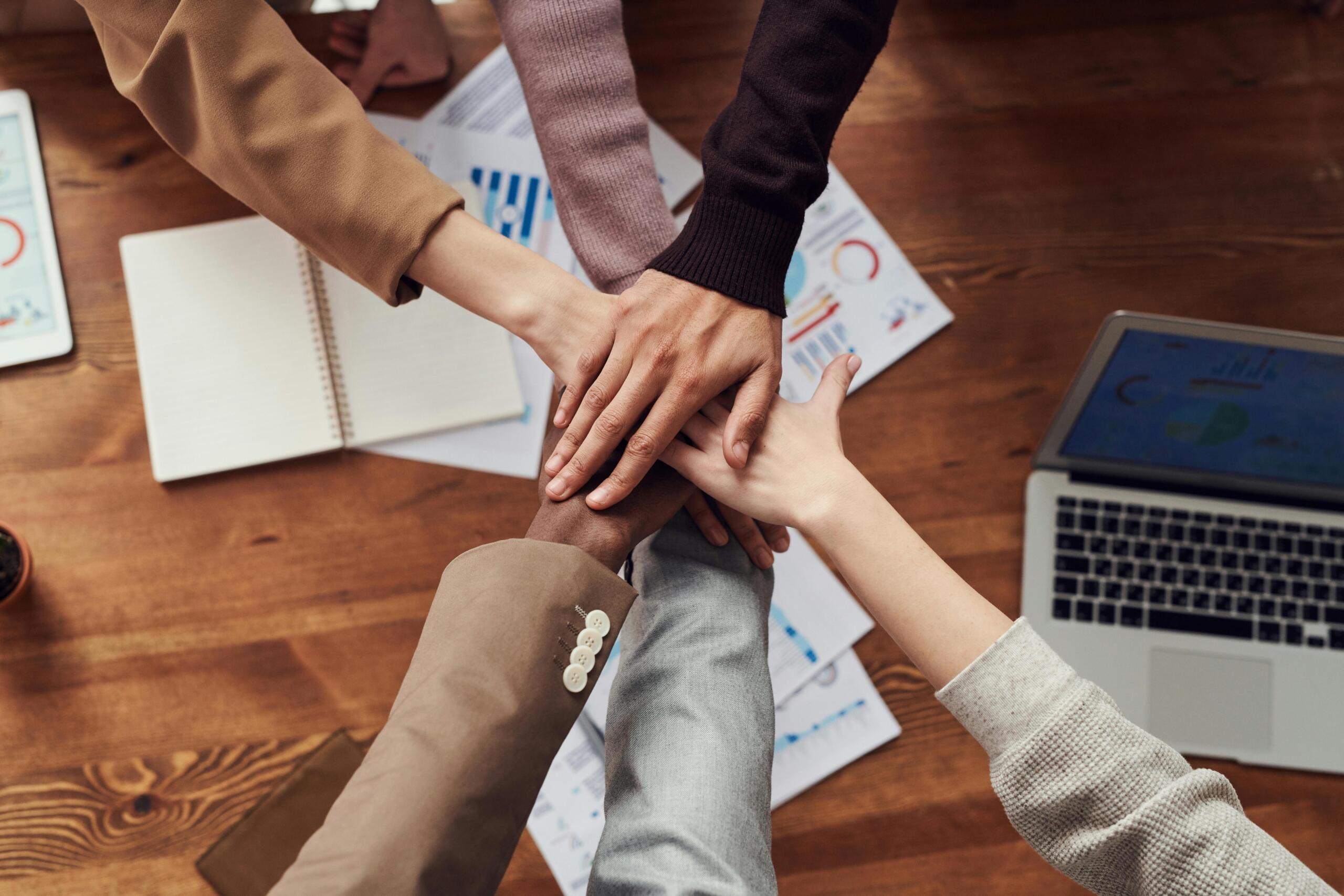 Diverse team members stacking hands over business documents and a laptop.