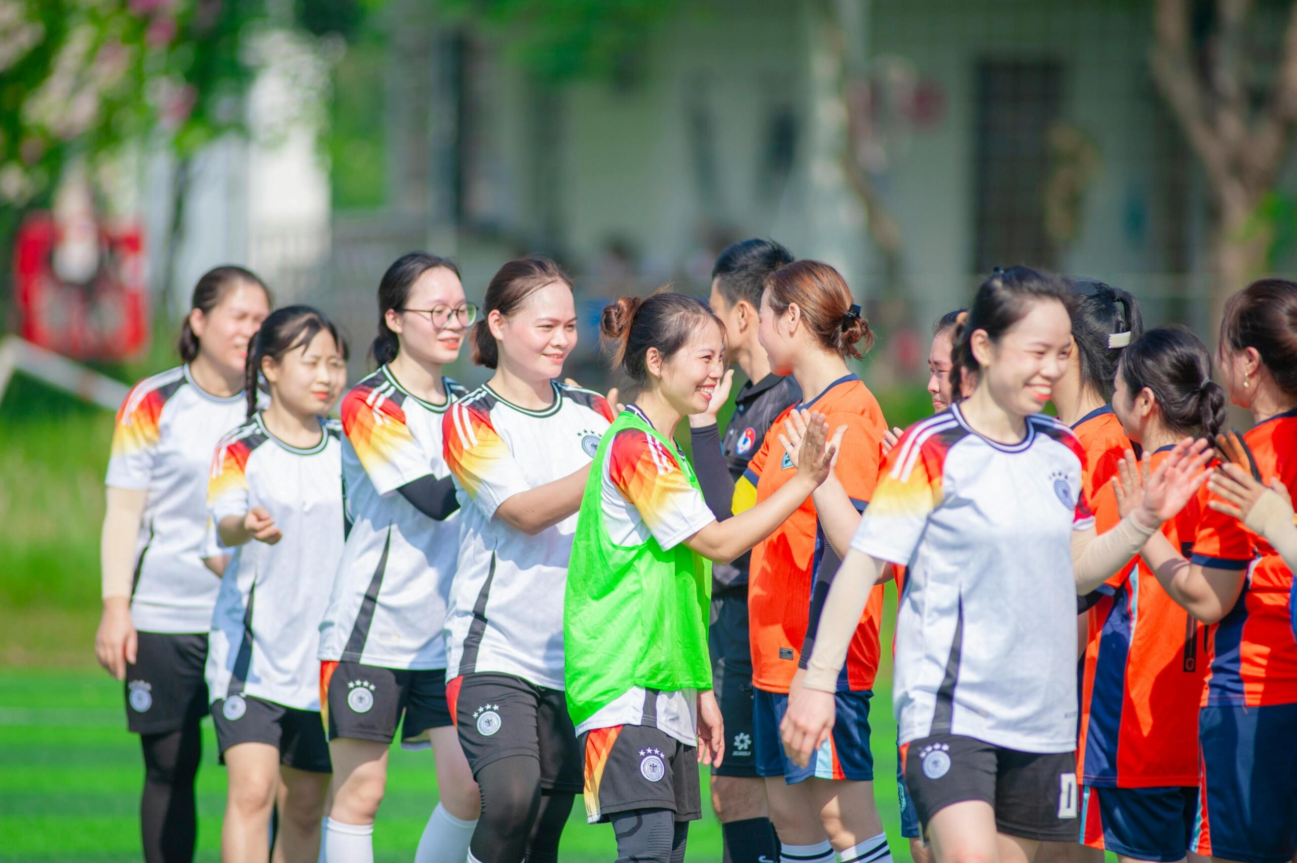 Women soccer players on a field, spaced out in formation, actively engaged in shaking hands.