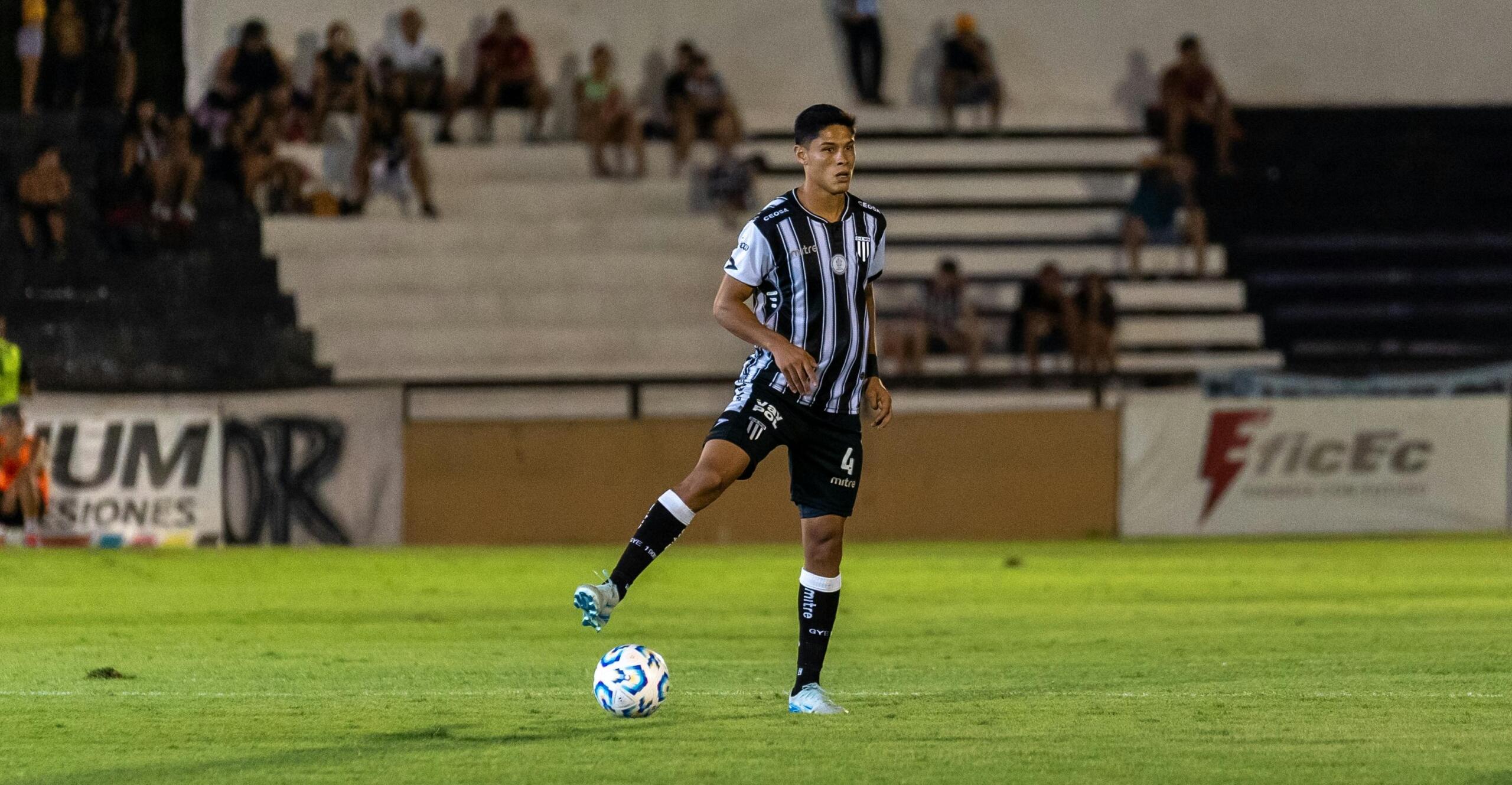 A soccer player standing confidently on the pitch with a ball positioned under one foot, dressed in a uniform and ready for action.